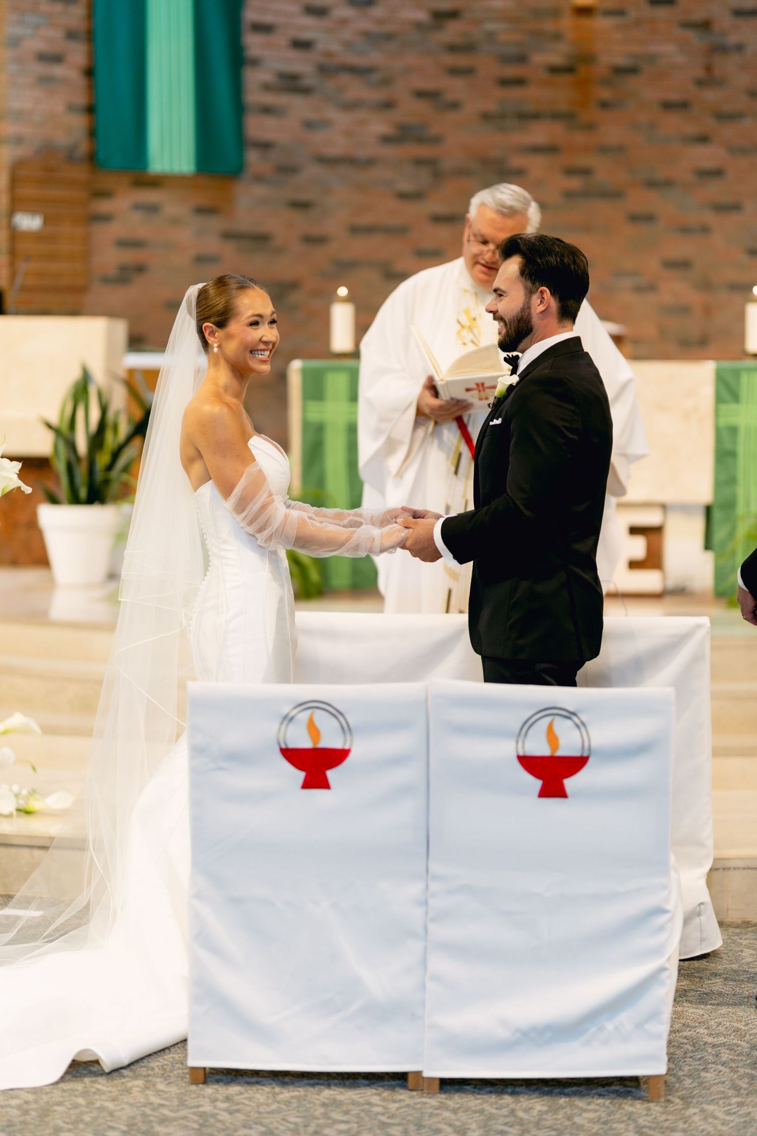 Smiling bride and groom exchanging vows at church altar with officiant during wedding ceremony.