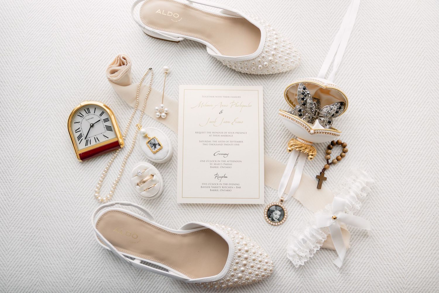Flat lay of bridal accessories including pearl shoes, garter, jewelry, clock, and elegant wedding invitation.