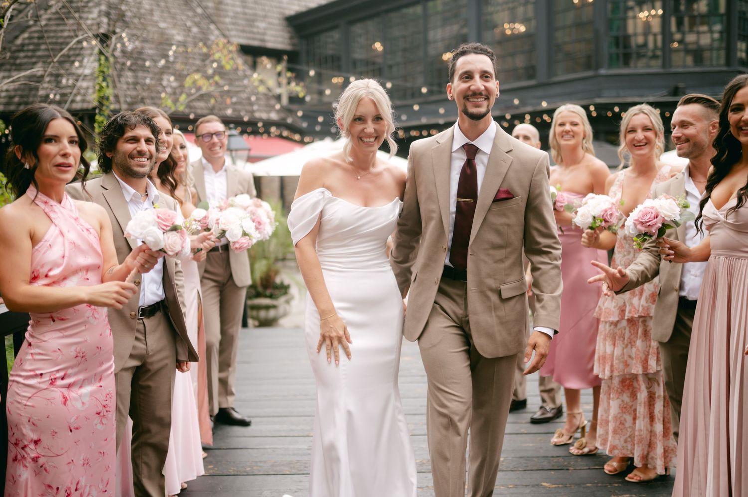 Wedding party in pink dresses and tan suits lined up outdoors.