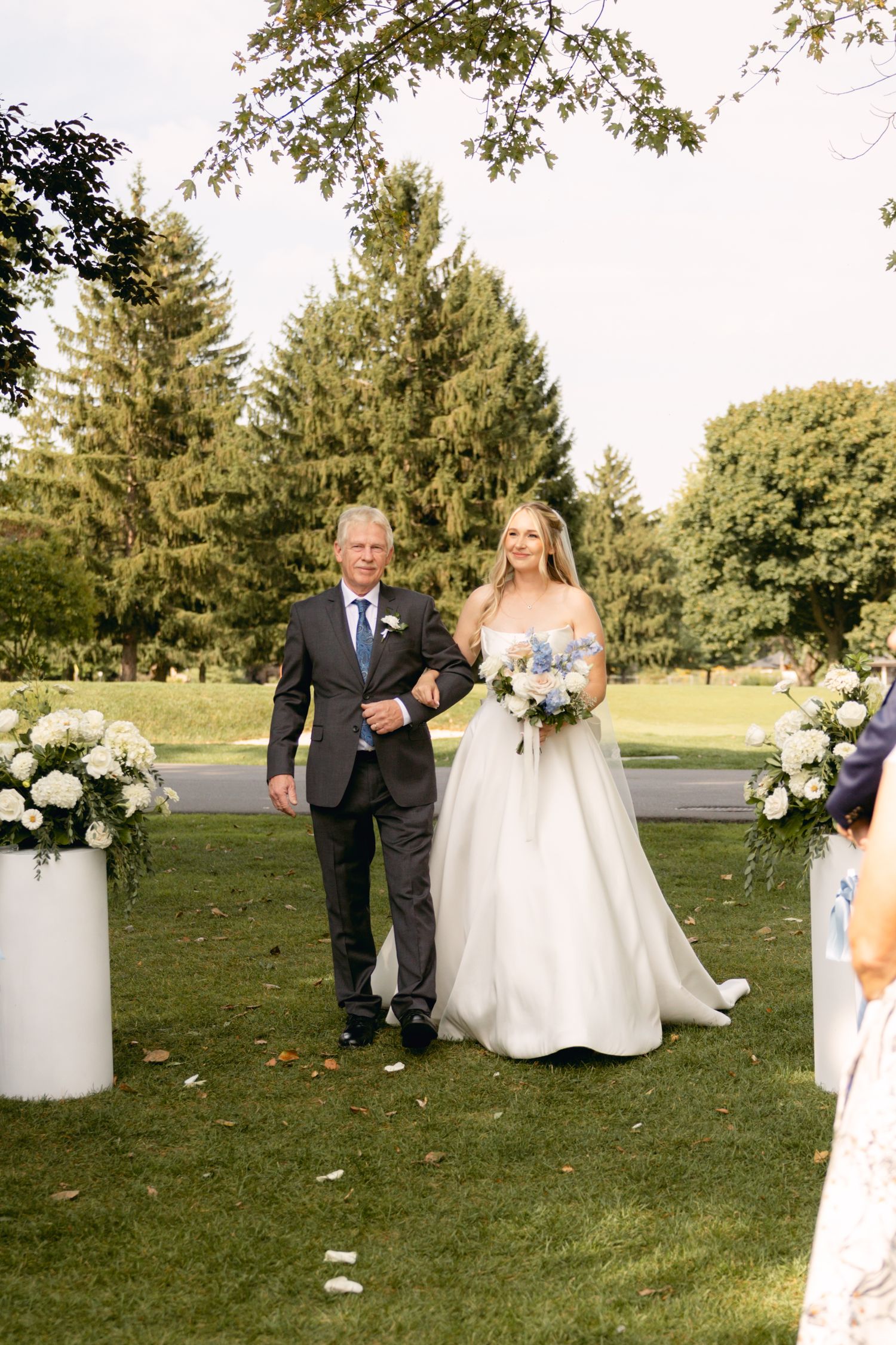 Wedding ceremony setup on grassy lawn with white floral arrangements and seating.