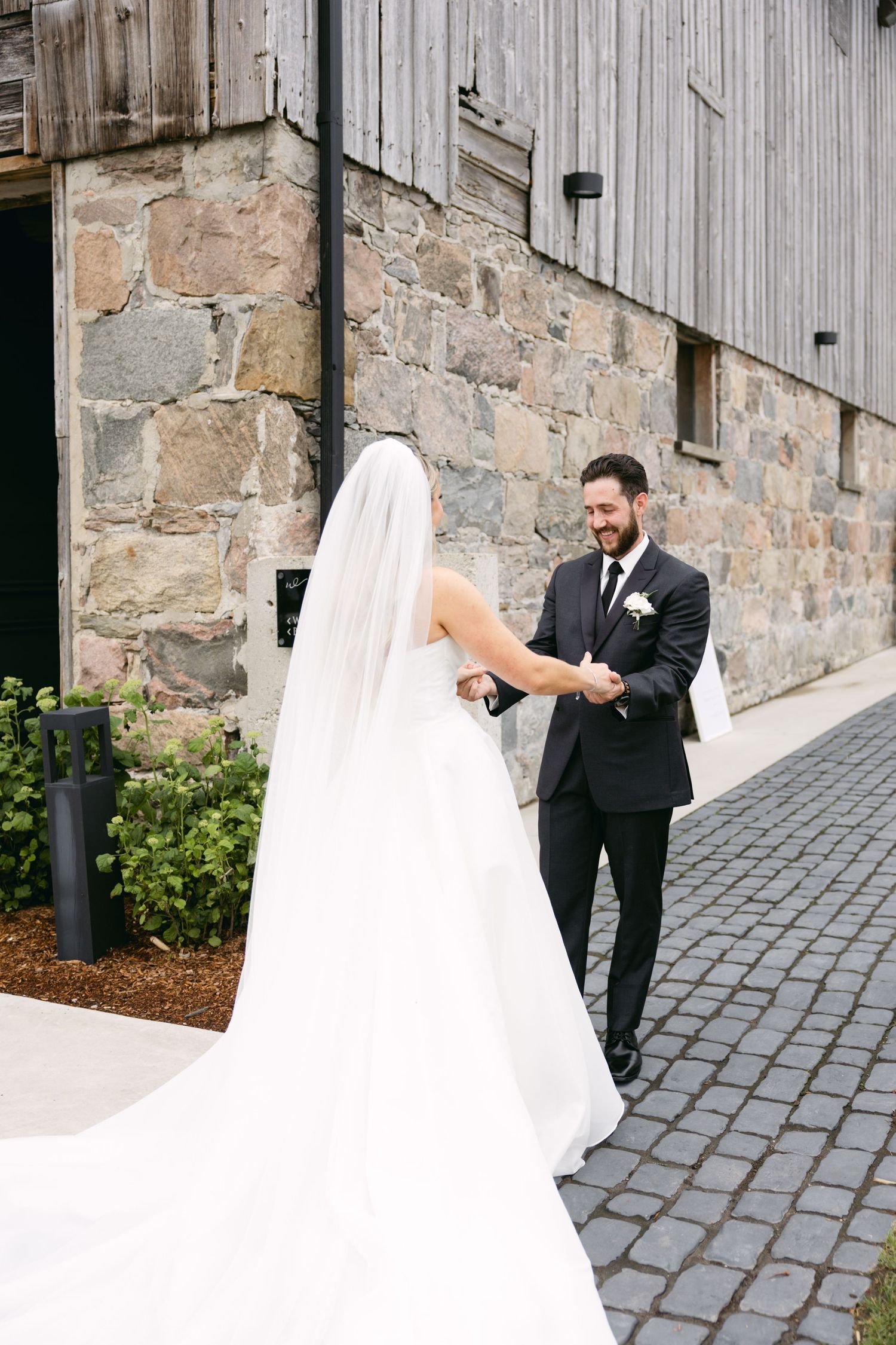 Wedding couple dancing on cobblestone path beside rustic stone building.