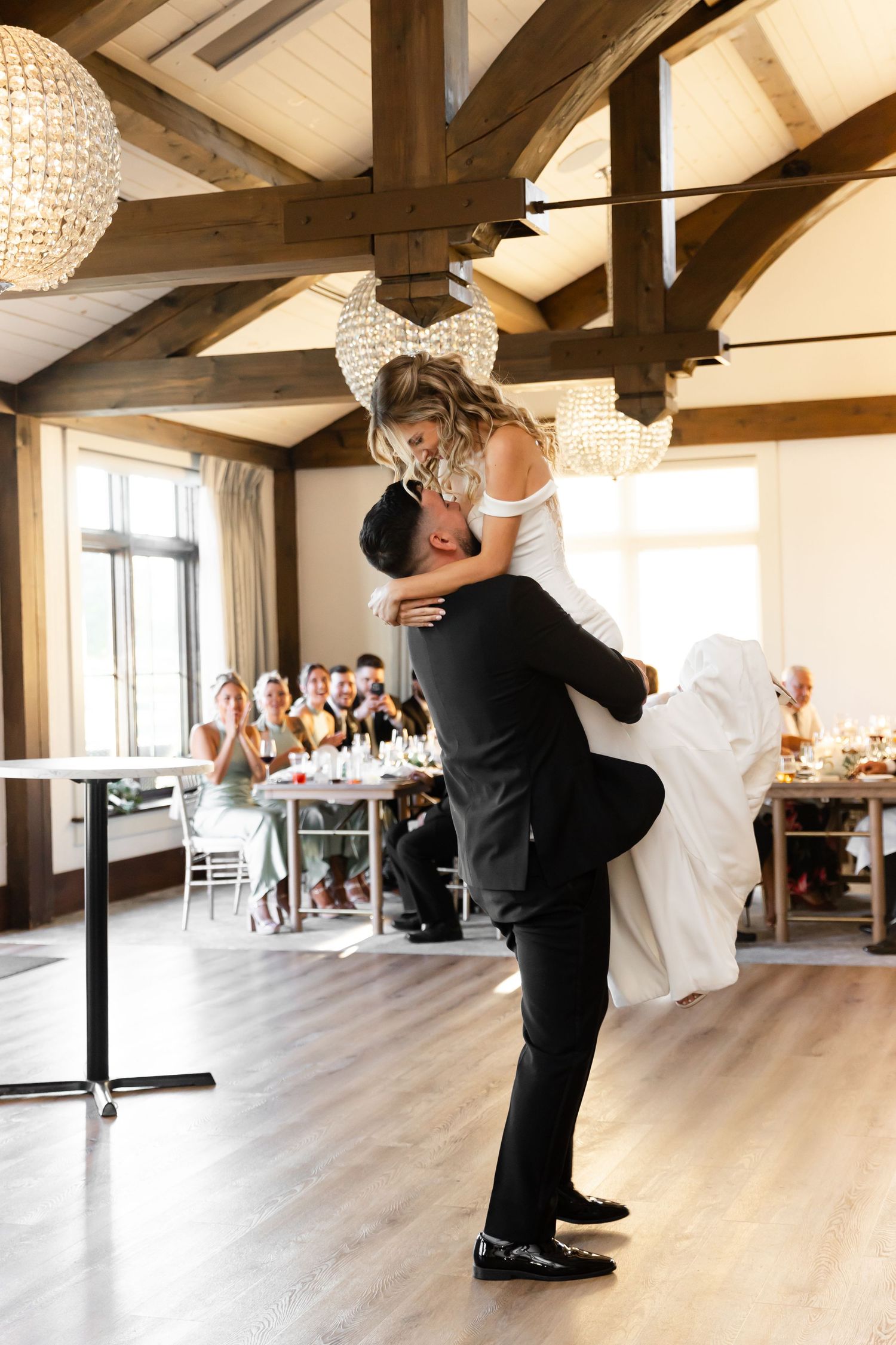 Romantic dance lift moment during wedding reception under crystal chandeliers.