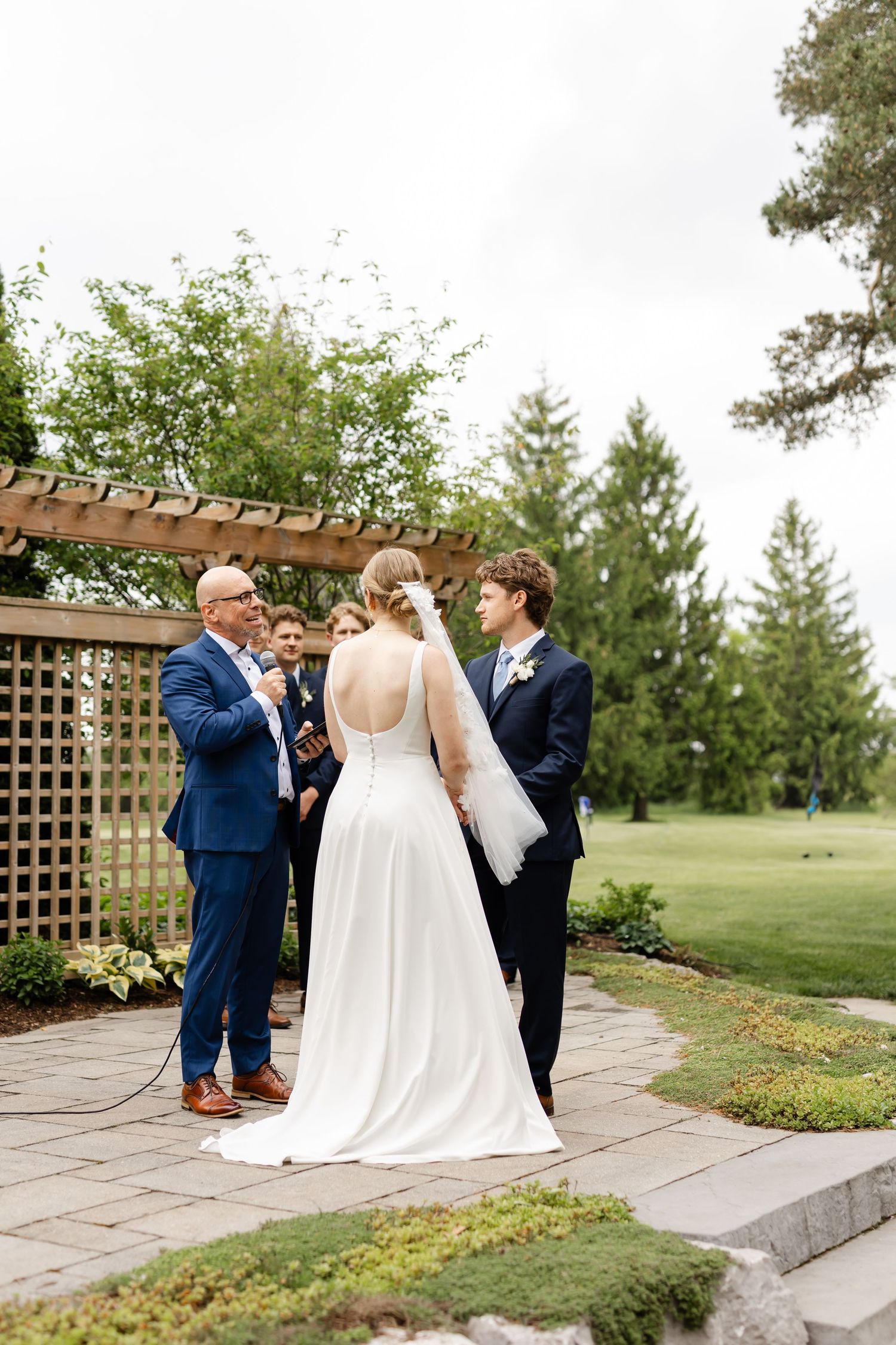 Wedding ceremony moment under wooden pergola in garden setting.