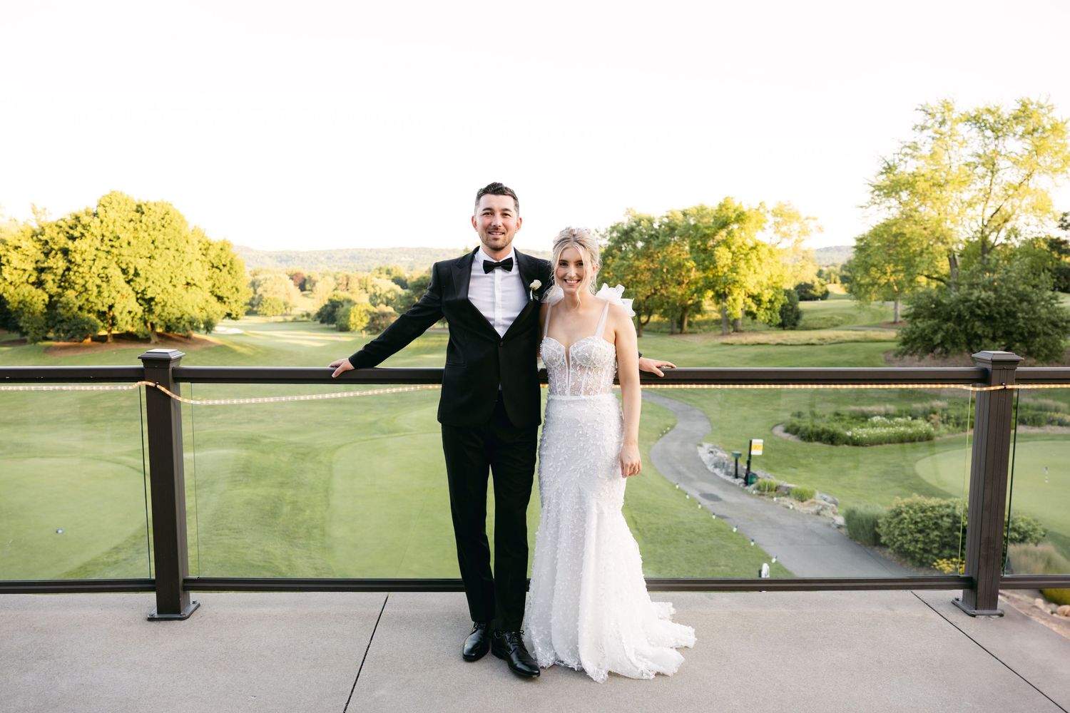 Wedding couple poses on a golf course with scenic paths and greenery in background.