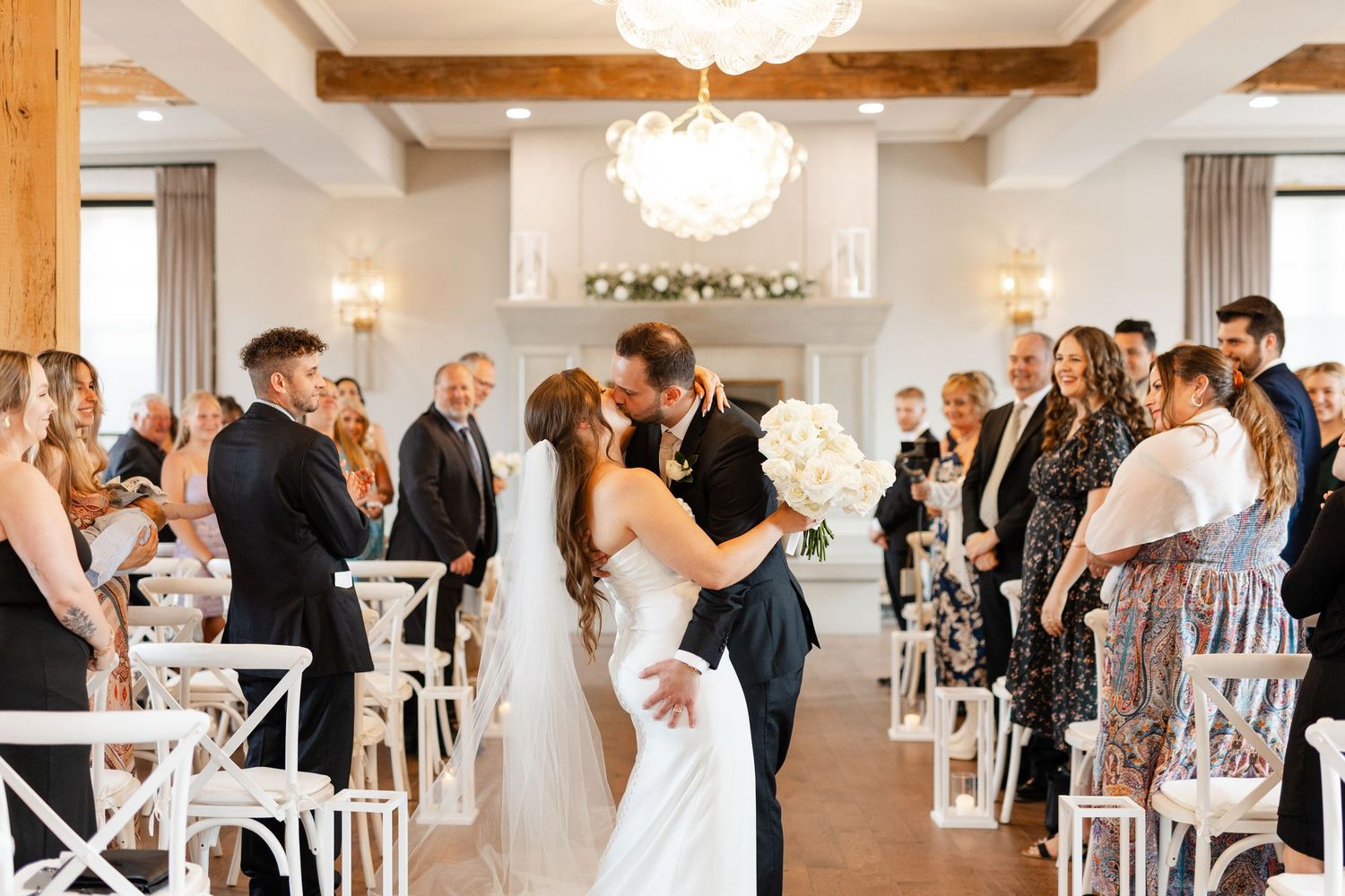 Bride and groom share their first kiss at the altar during an elegant indoor wedding ceremony.