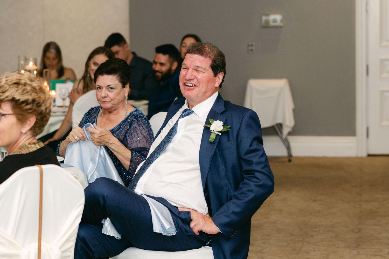 Wedding guests enjoying reception speeches in an elegant venue setting.