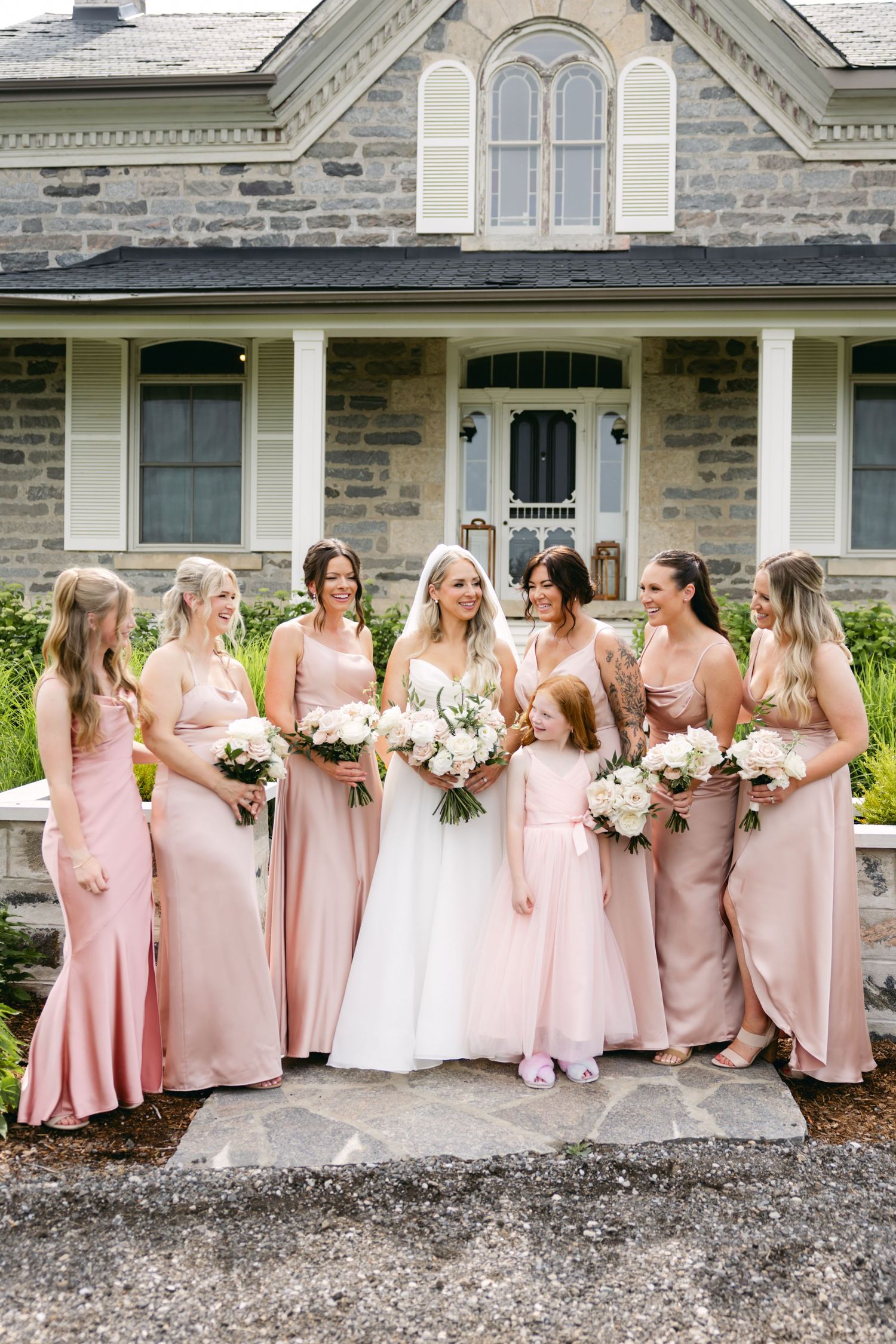 Wedding party in coordinating pink dresses arranged in front of elegant stone mansion.