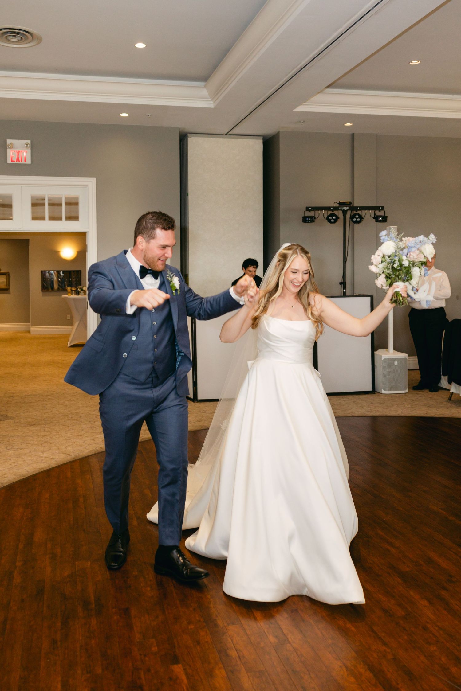 A couple dances together during their first dance in a beautiful reception hall with hardwood floors.