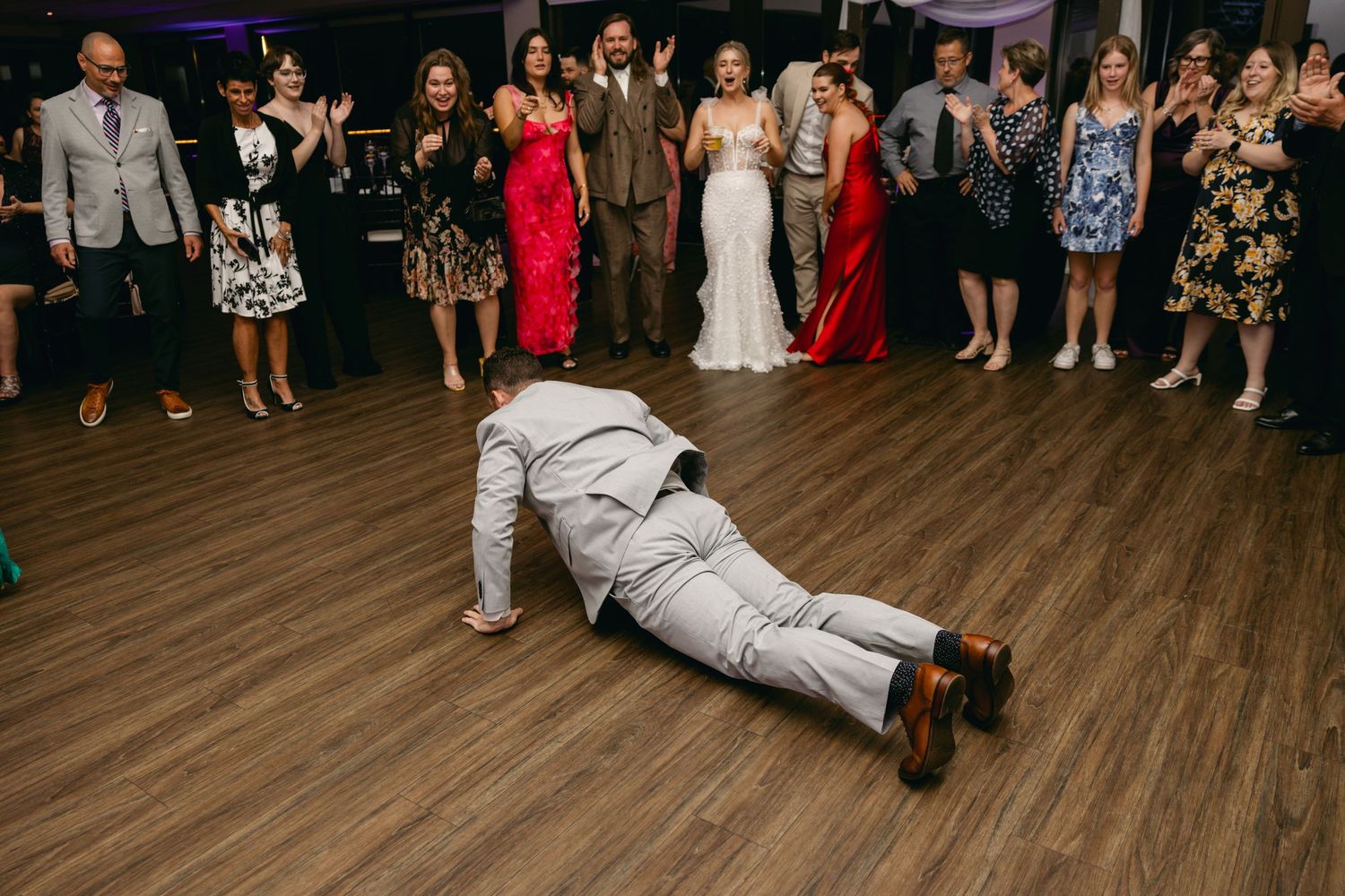 Wedding guests forming a dance circle during reception celebration on wooden floor.