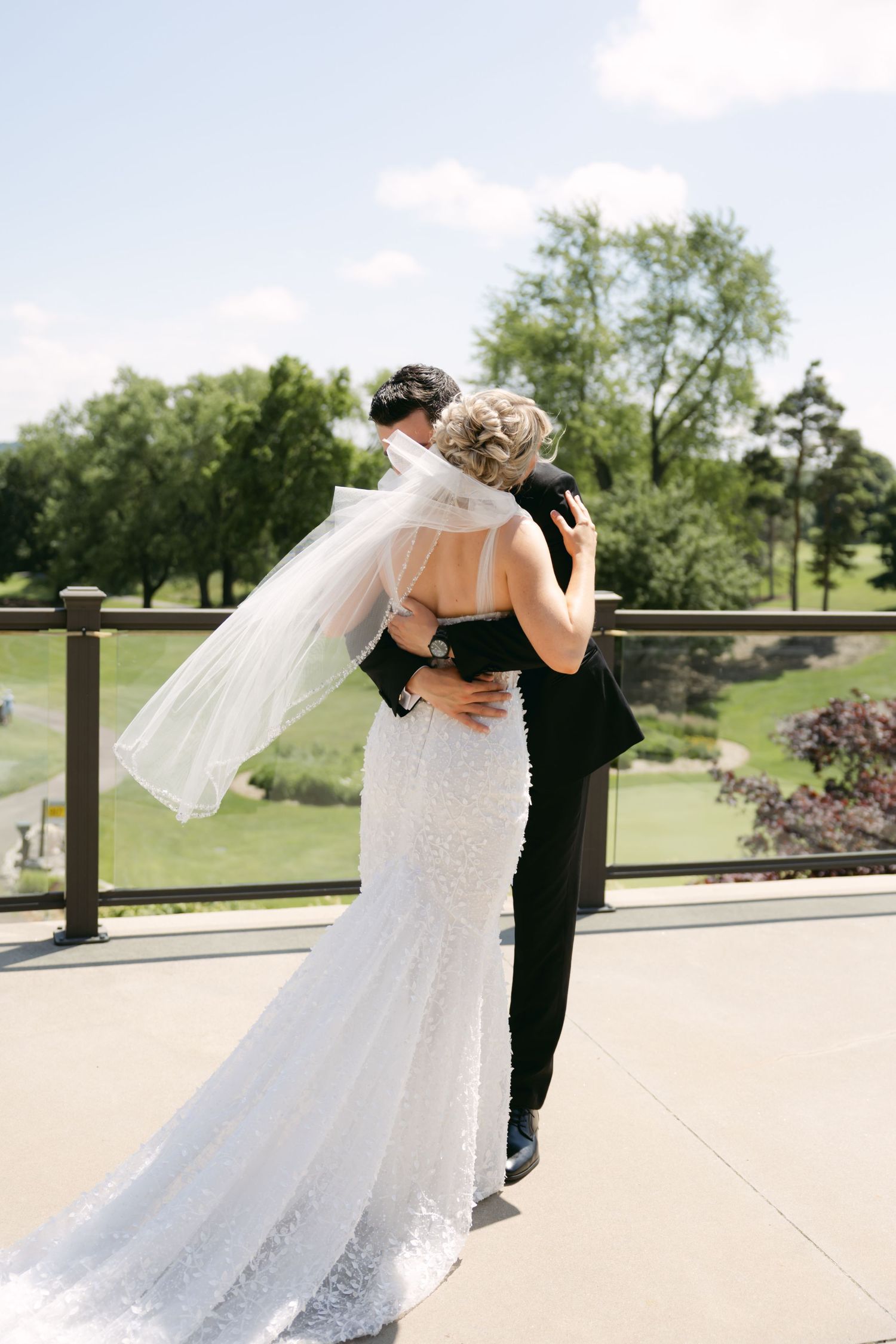 Couple embraces on outdoor terrace with scenic golf course view on sunny day.