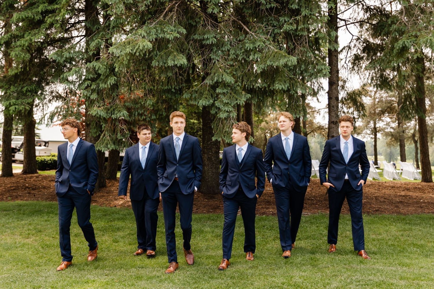 Group of men in navy suits run and jump across a grassy lawn during wedding photos.