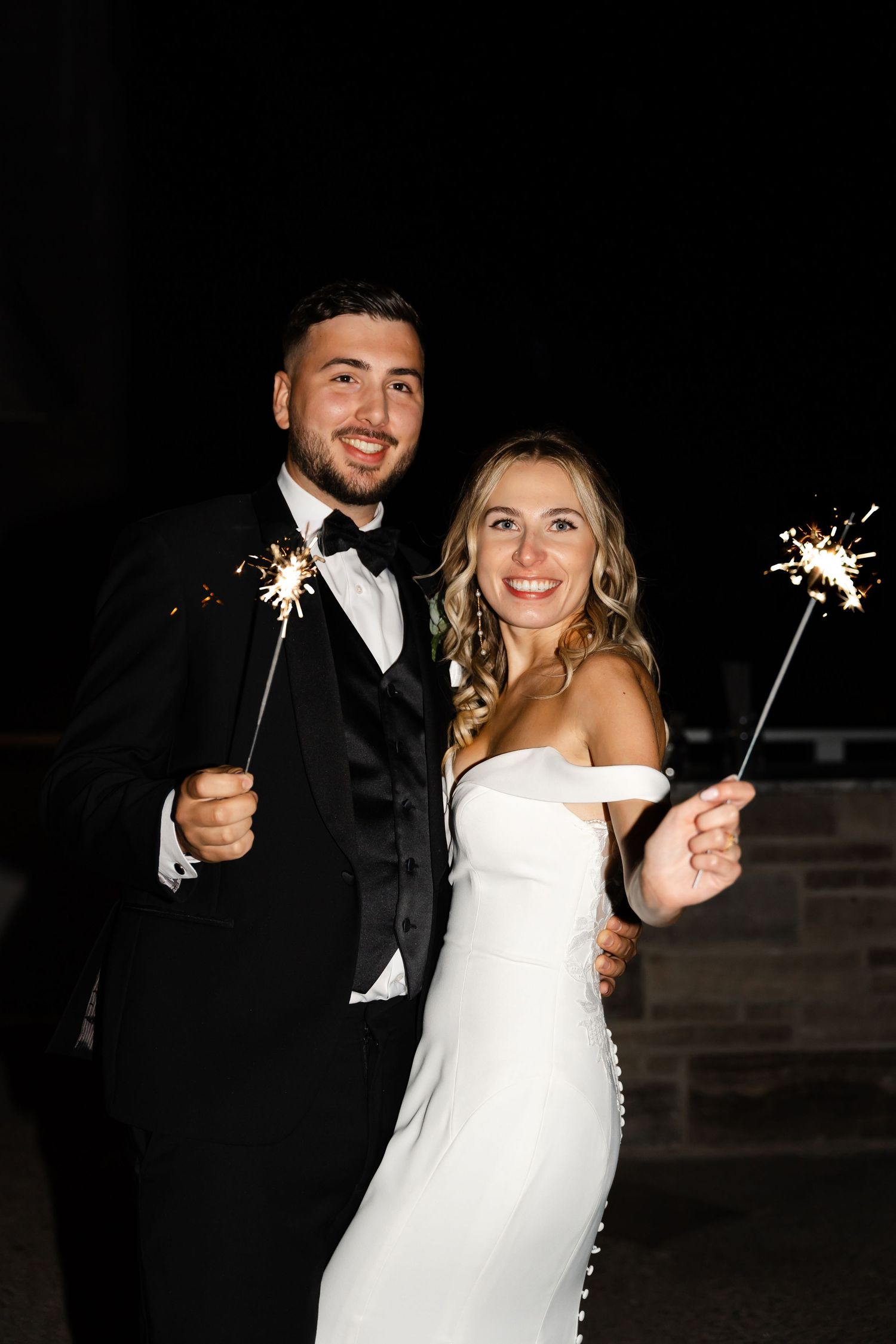 Newlyweds share joyful moments while holding sparklers during nighttime wedding celebrations.