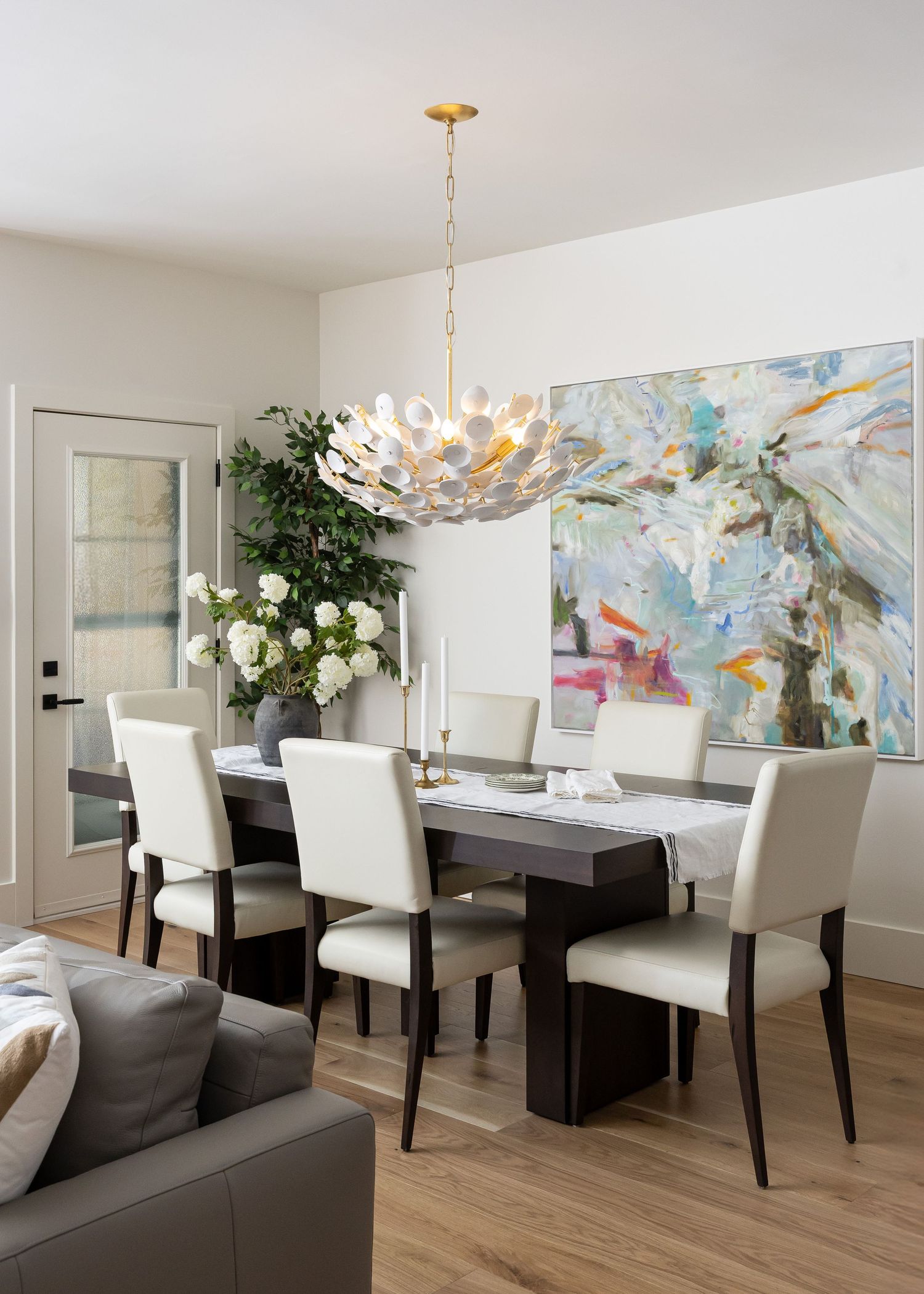 Elegant dining room with abstract art, statement chandelier, and white upholstered chairs.