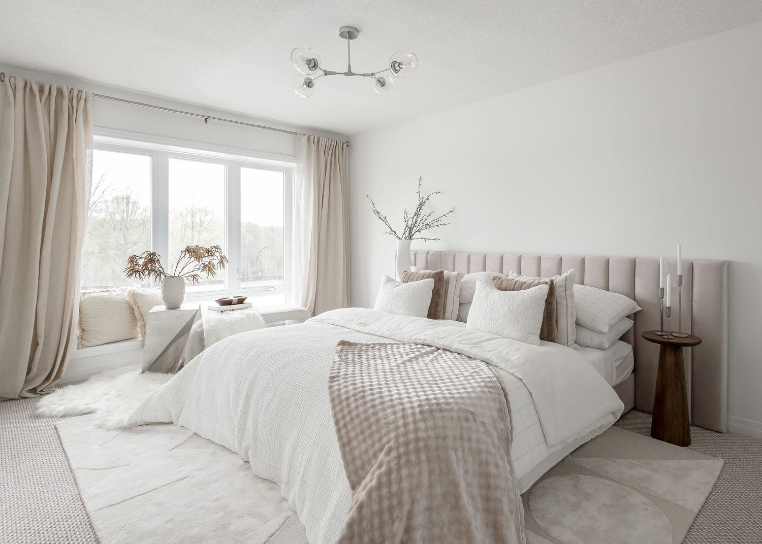 Bright master bedroom with beige accents, floor-to-ceiling windows, and modern lighting.