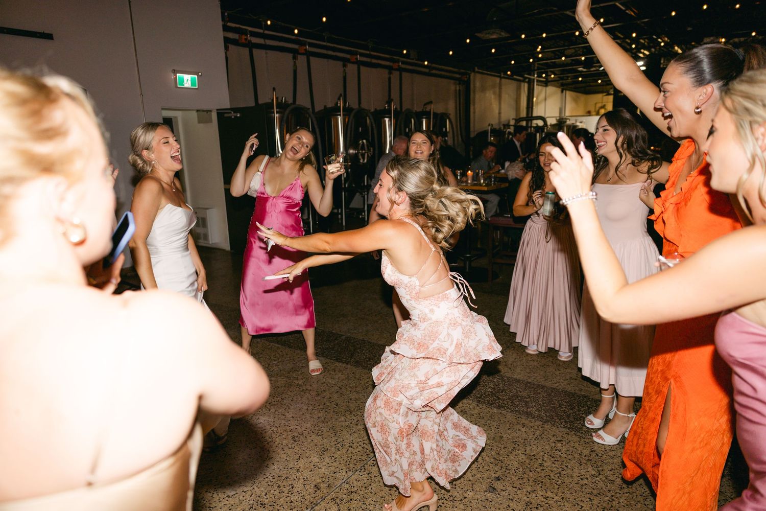 Lively dance floor scene at a wedding reception with guests dancing under indoor lighting.