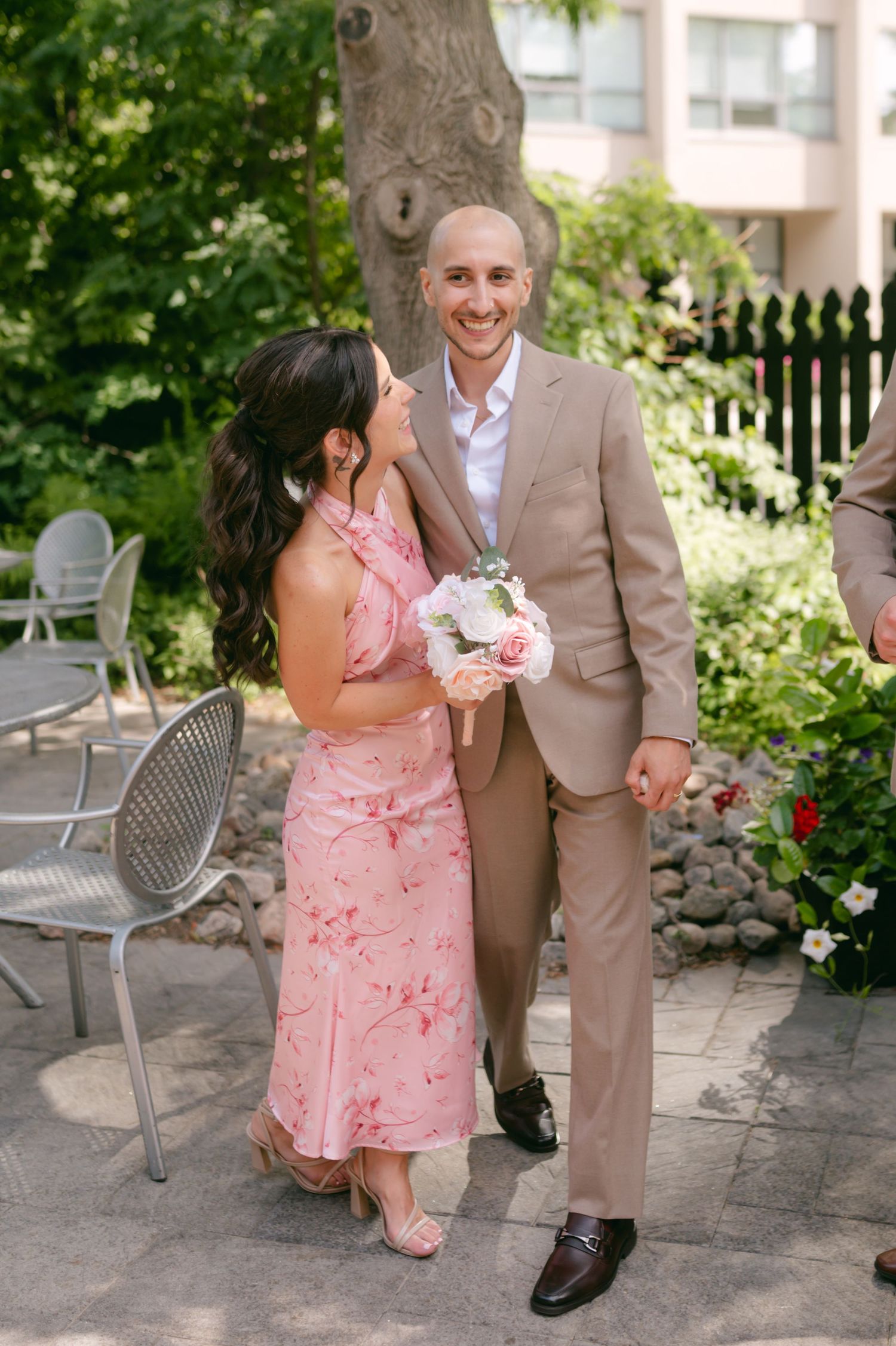 Couple in pink dress and tan suit pose together in a garden setting.