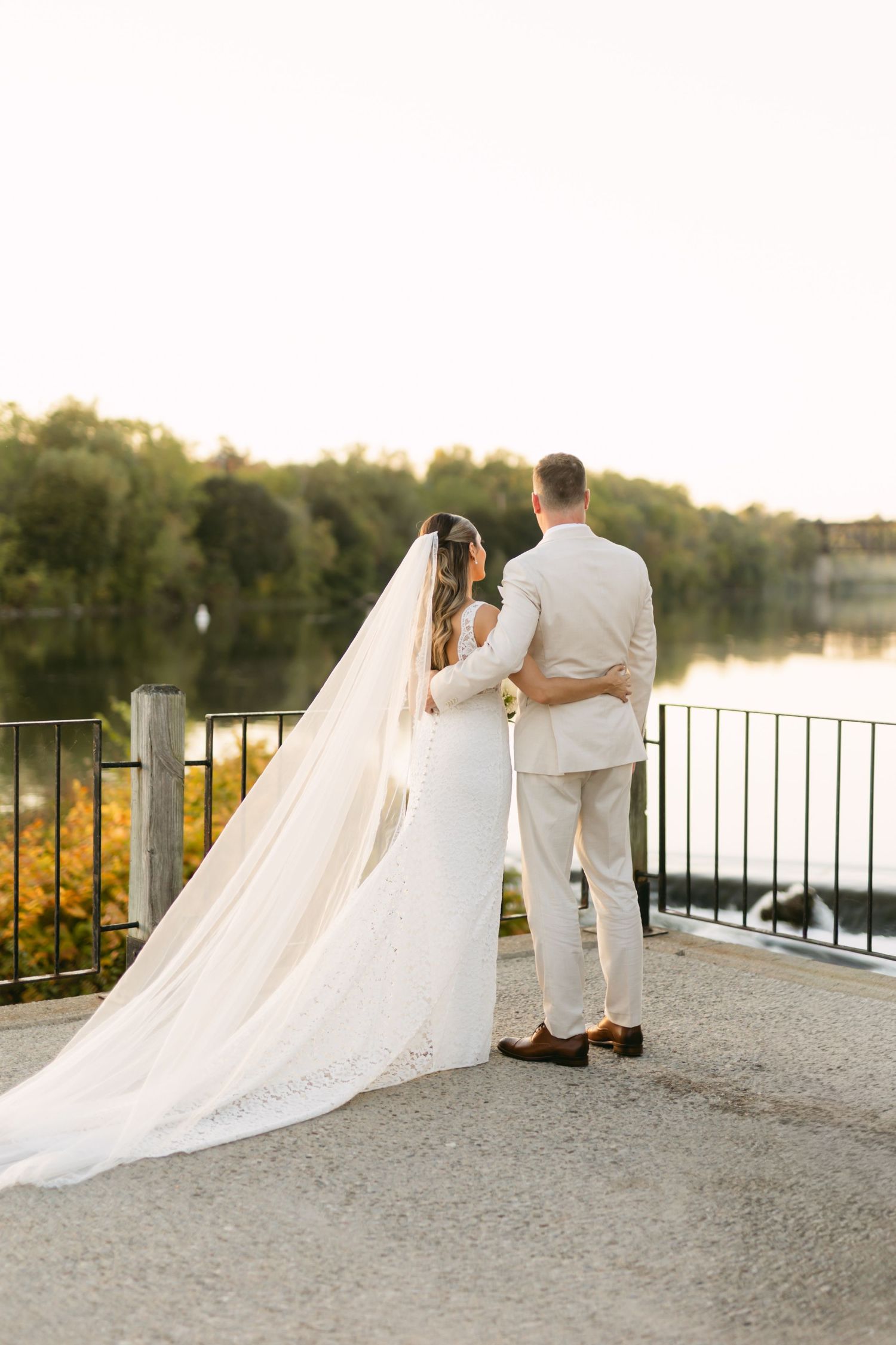 Newlyweds share romantic moments on lakeside terrace with long flowing veil.