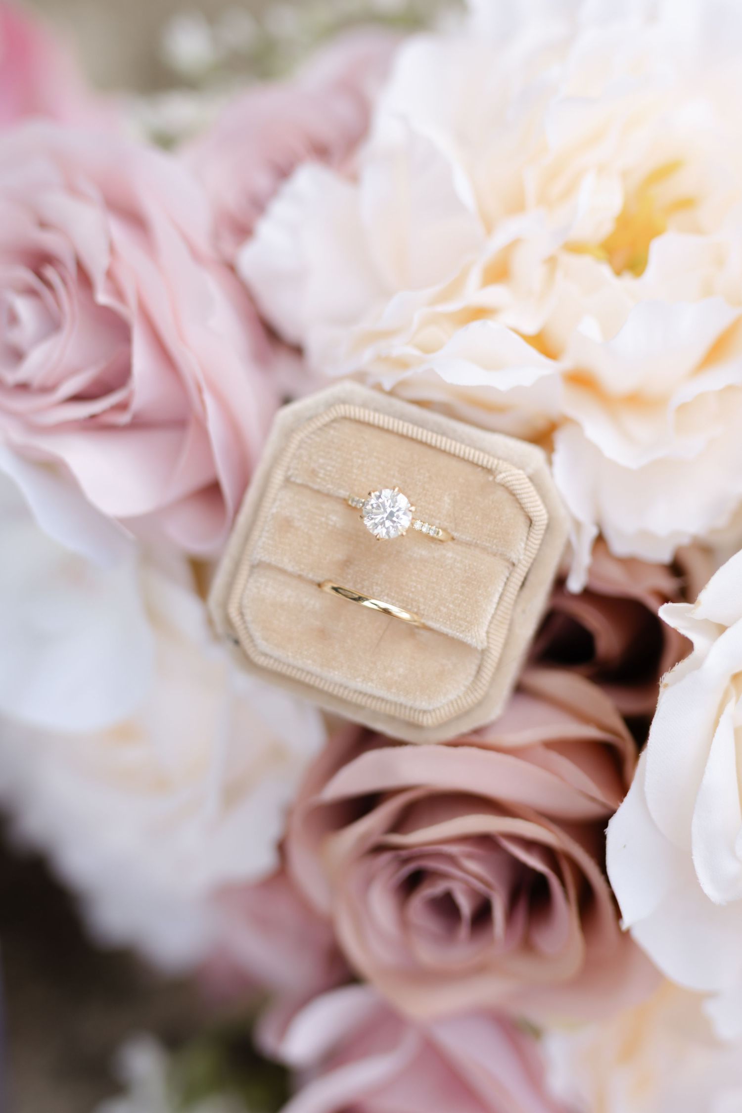 A sparkling diamond engagement ring nestled in a beige velvet ring box with pink roses.