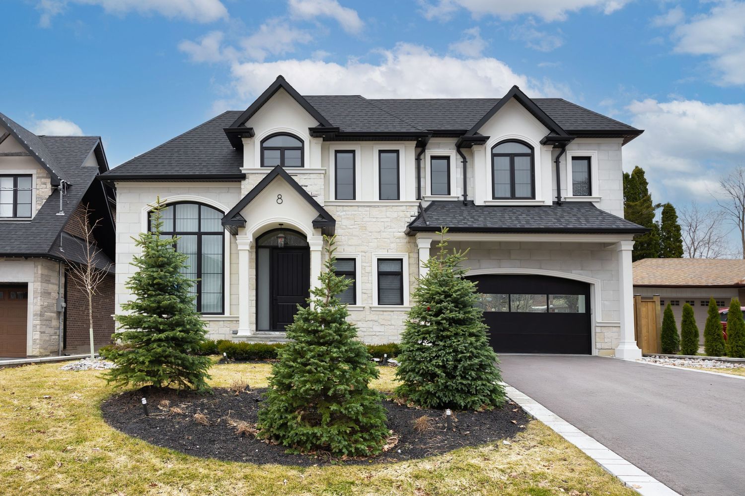 Modern luxury home exterior with black and white color scheme and large driveway under blue sky.