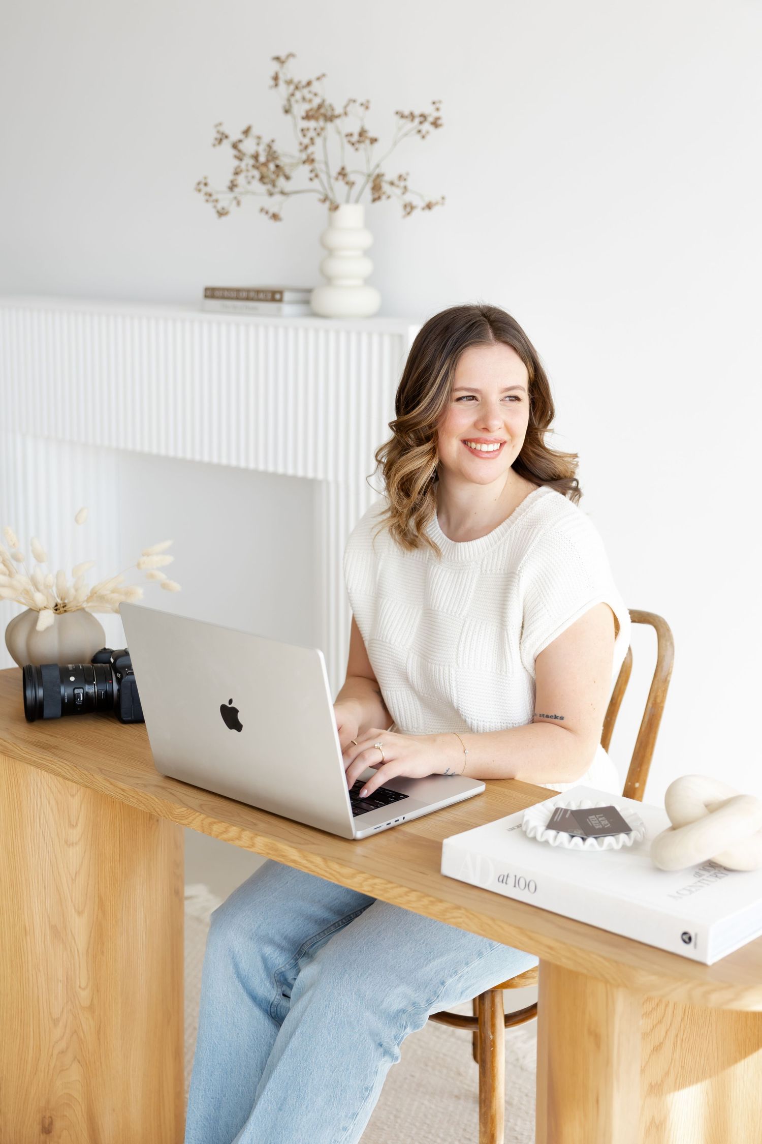 Modern workspace setup with laptop, camera gear and minimalist decor in bright white room.