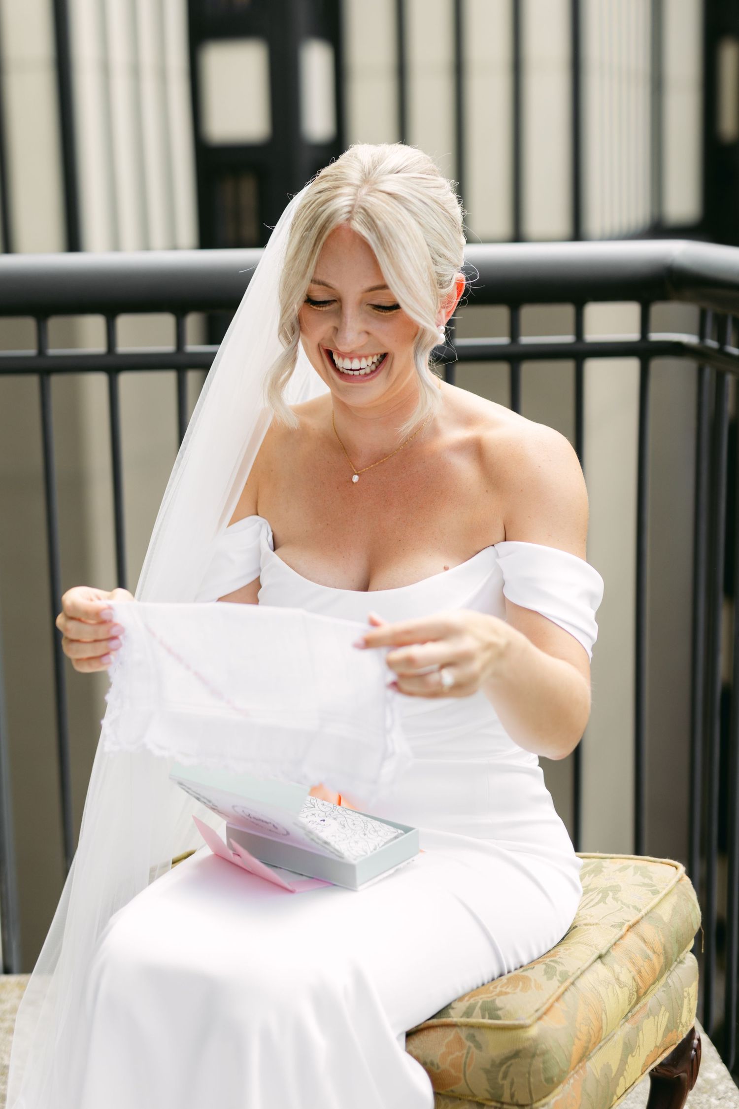 Bride in white dress reading letters while sitting outdoors on a sunny day.