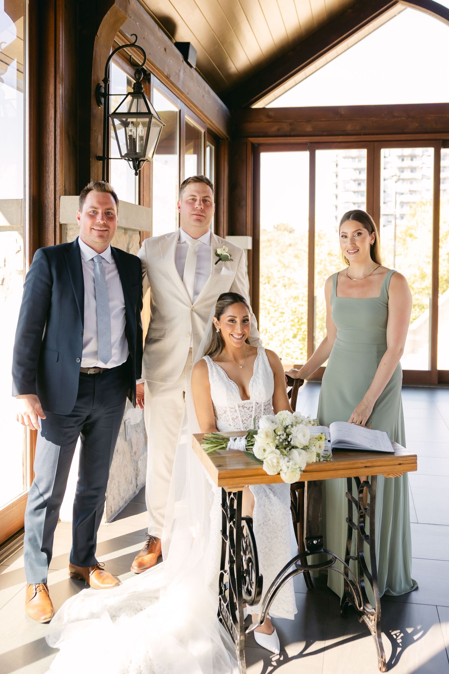 Wedding party poses together in elegant attire against rustic wooden interior.