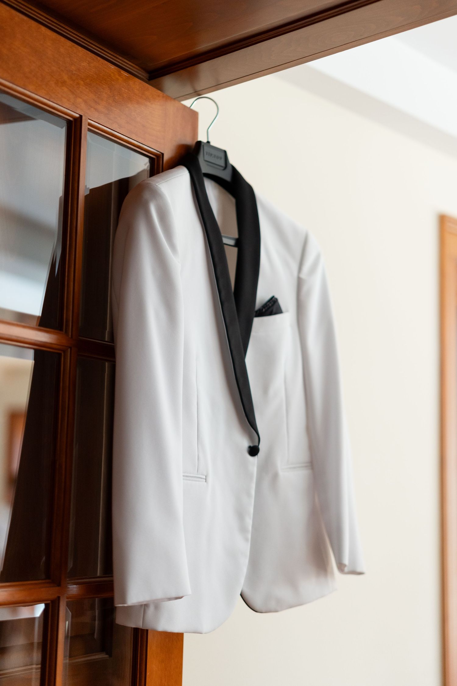 White tuxedo jackets with black lapels hanging neatly on wooden hangers.