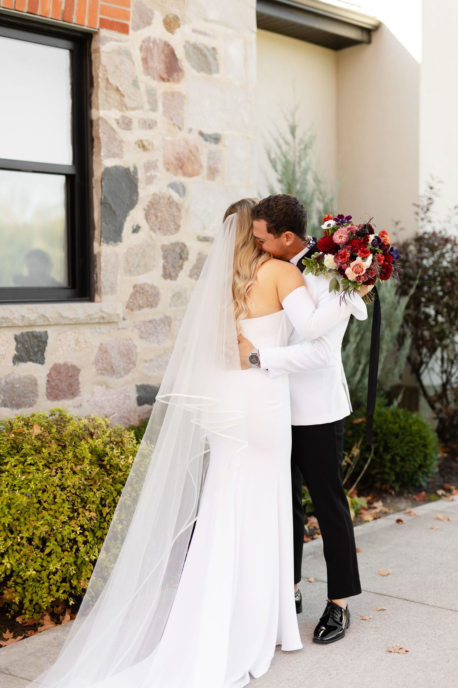 An emotional first look embrace between newlyweds against a stone wall backdrop.