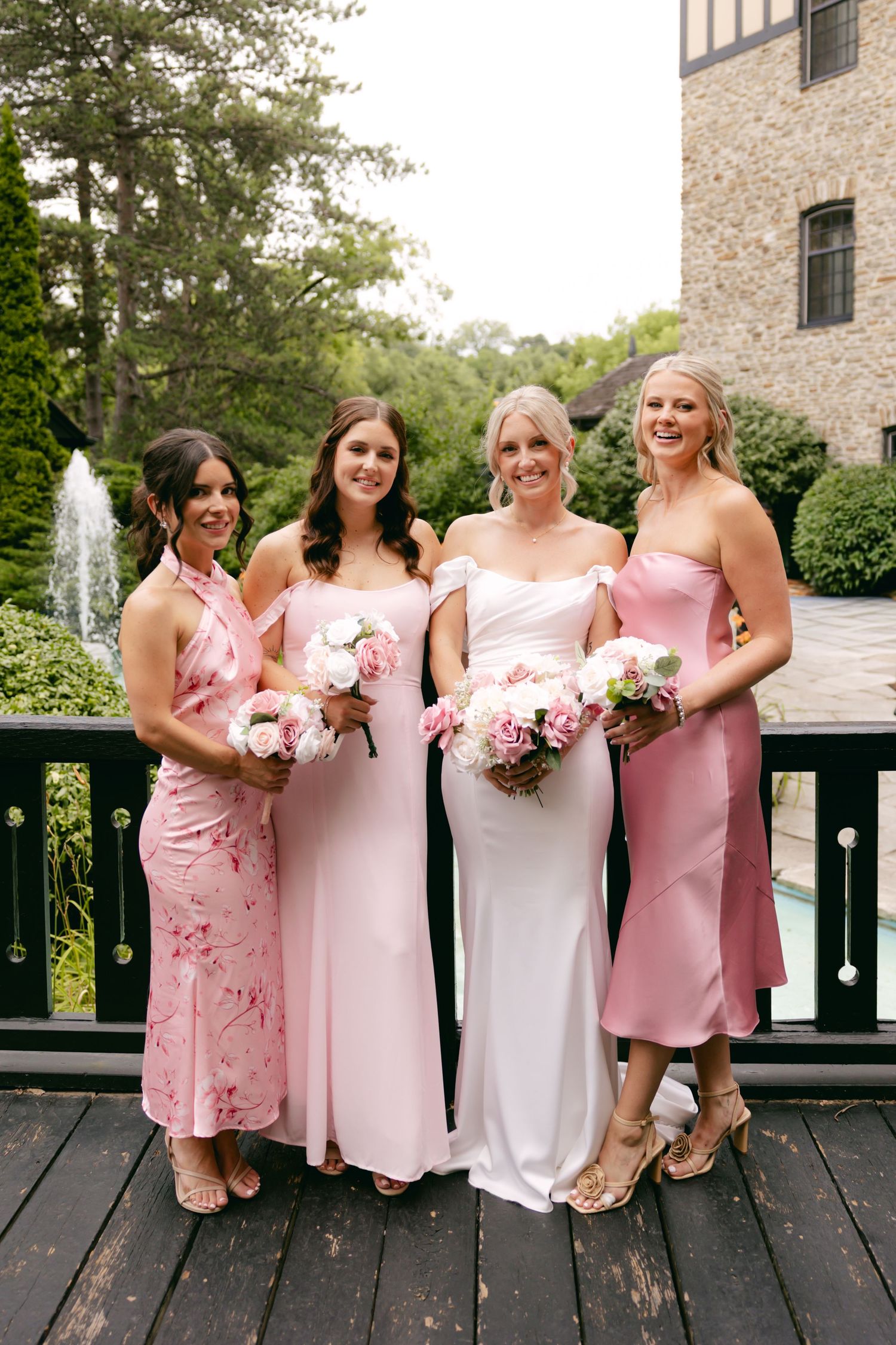 Bridesmaids lined up on a deck wearing various shades of pink dresses and holding bouquets.