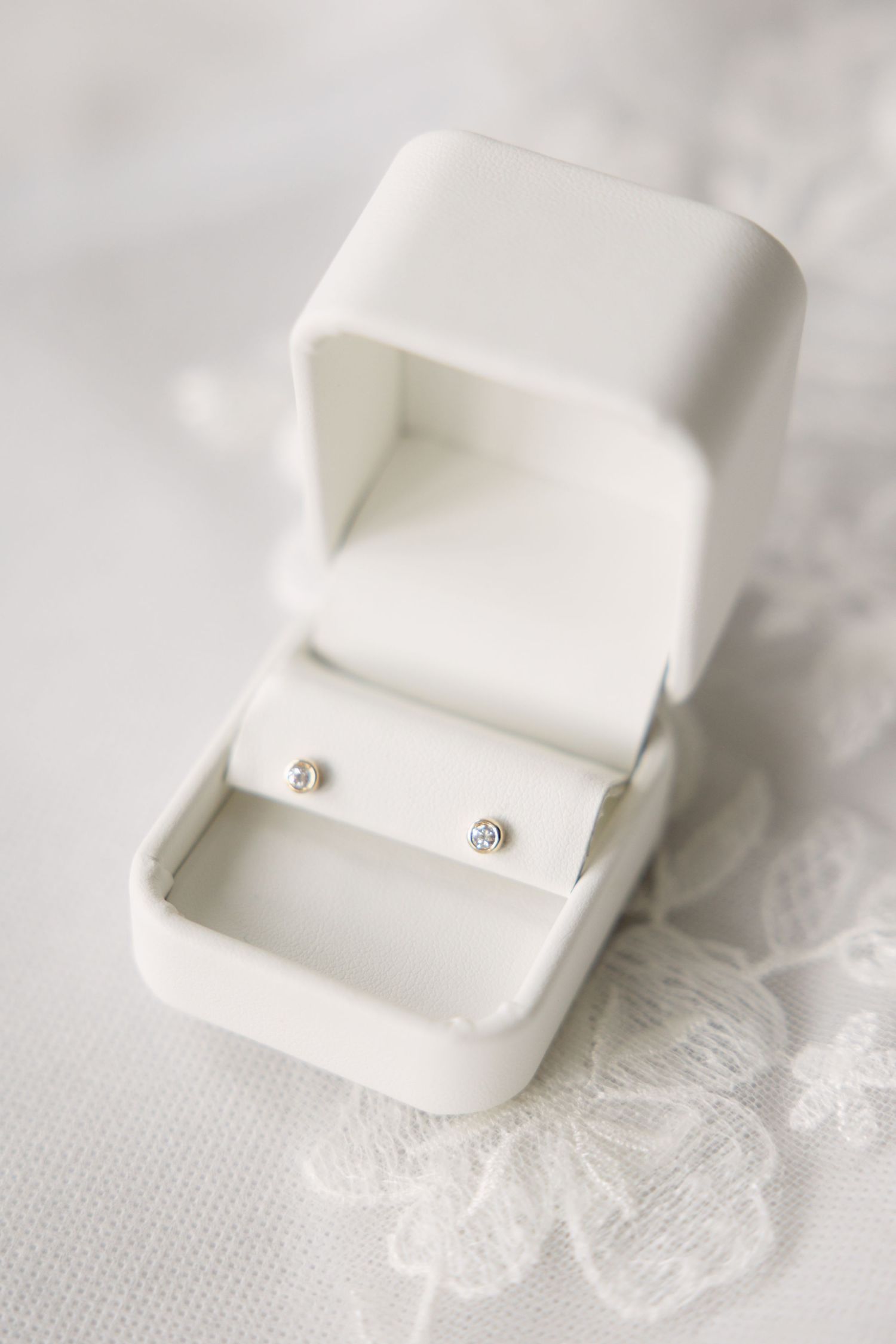 Close-up of a white ring box with small diamond studs on delicate lace fabric.
