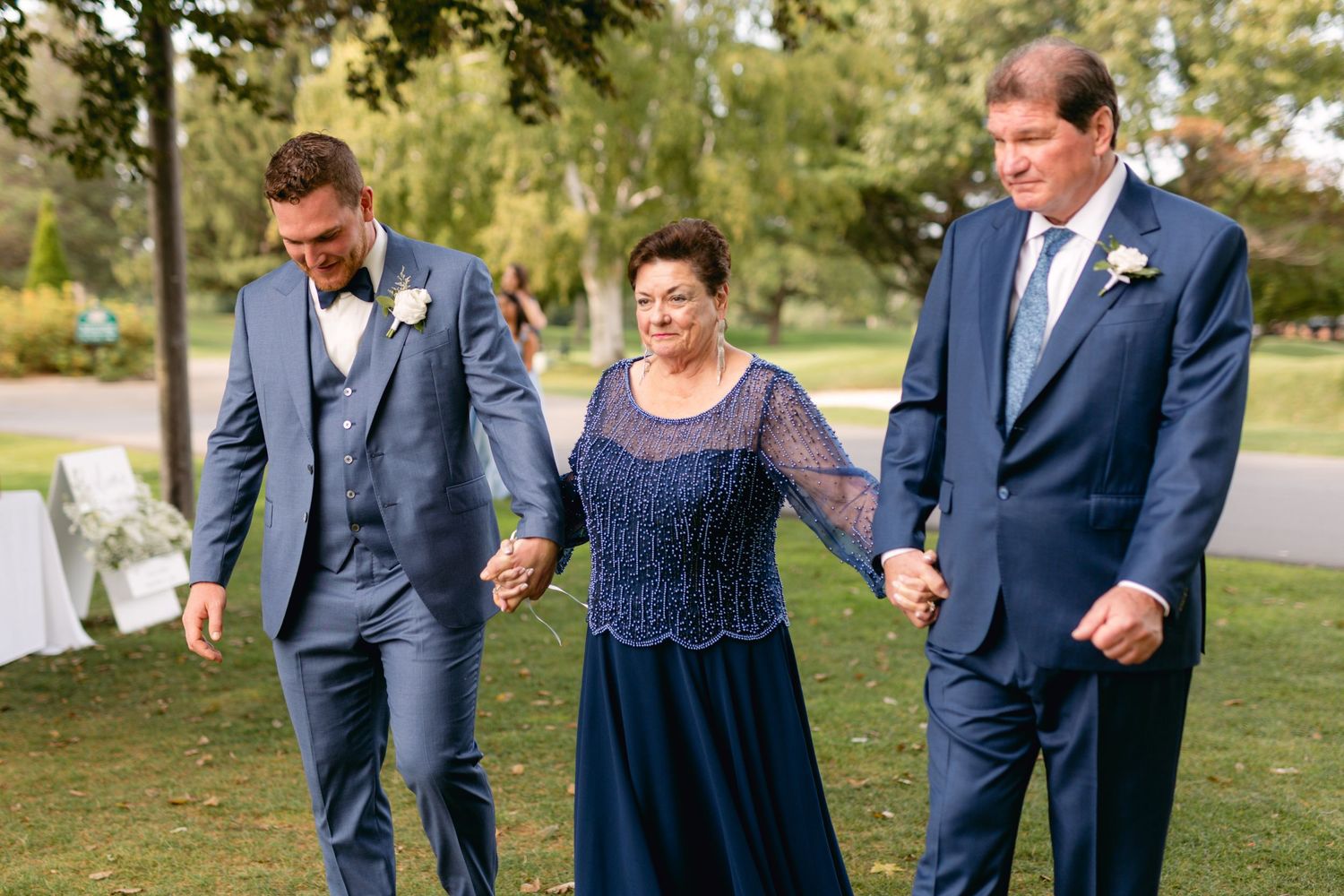 Wedding party members walk together on grass during outdoor celebration.