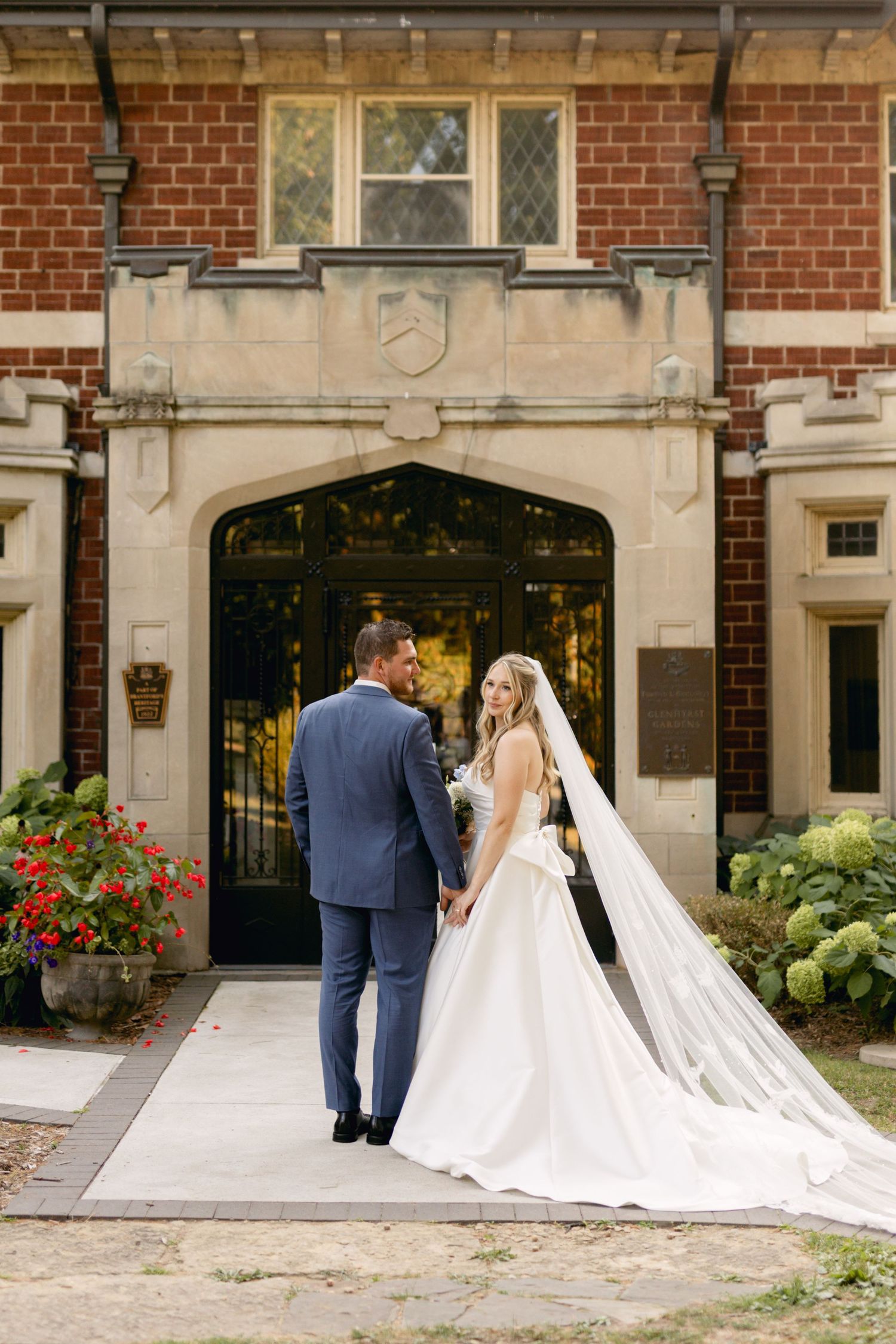 Bride and groom walk towards ornate brick entrance of historic building.
