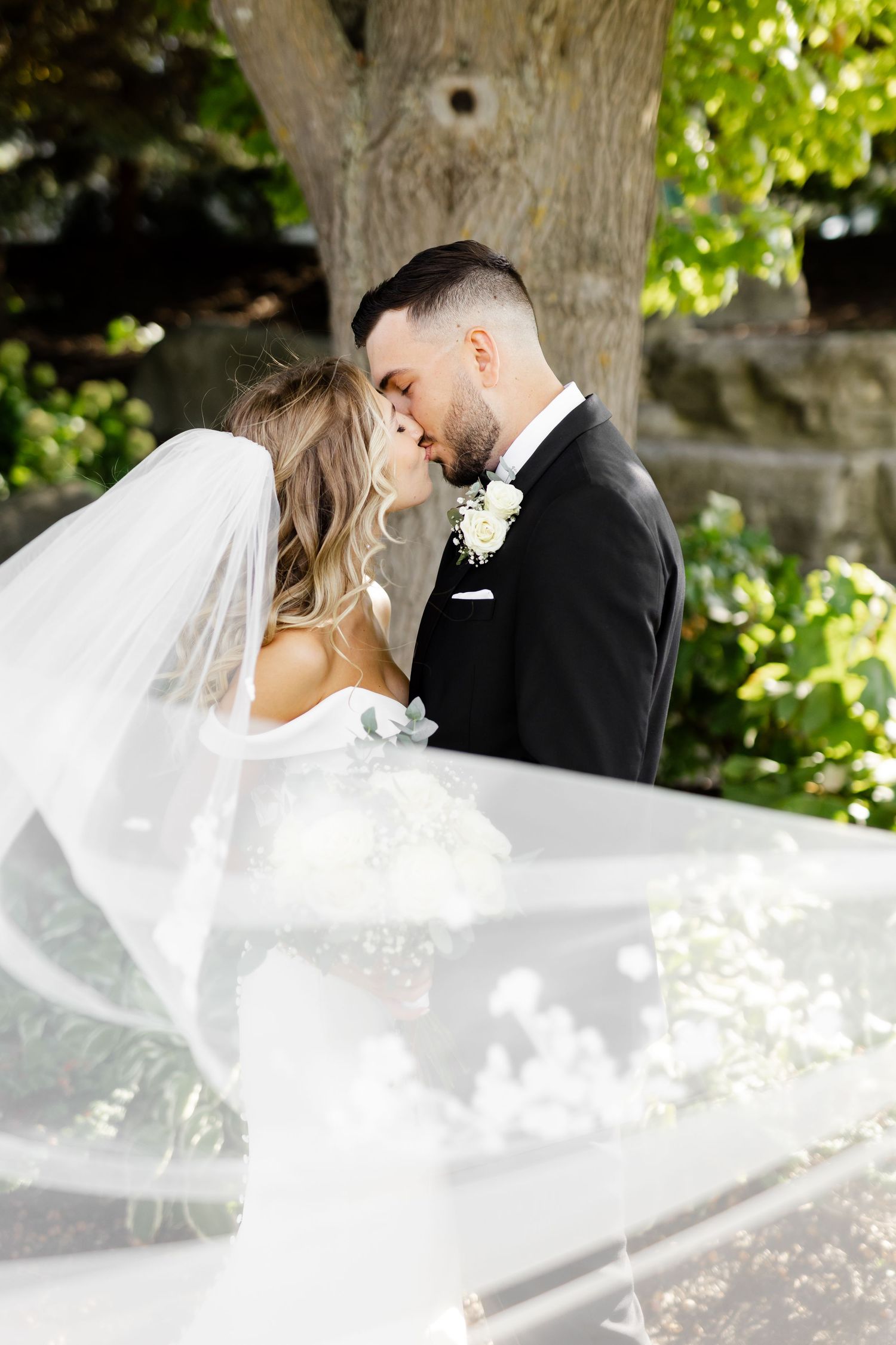 Intimate wedding portrait with flowing veil and natural outdoor lighting.