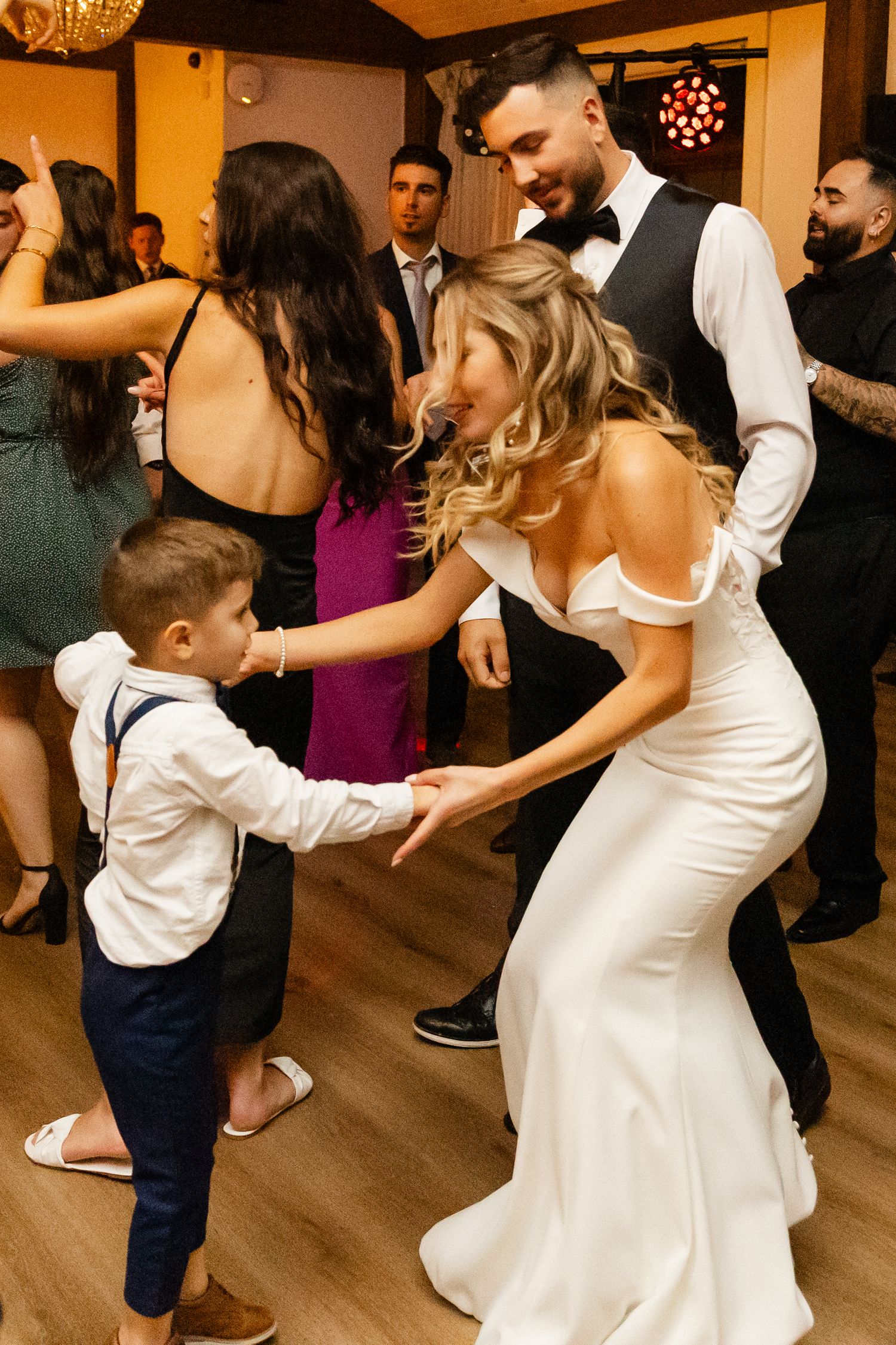 Wedding guests dancing together on a wooden dance floor at an indoor reception.