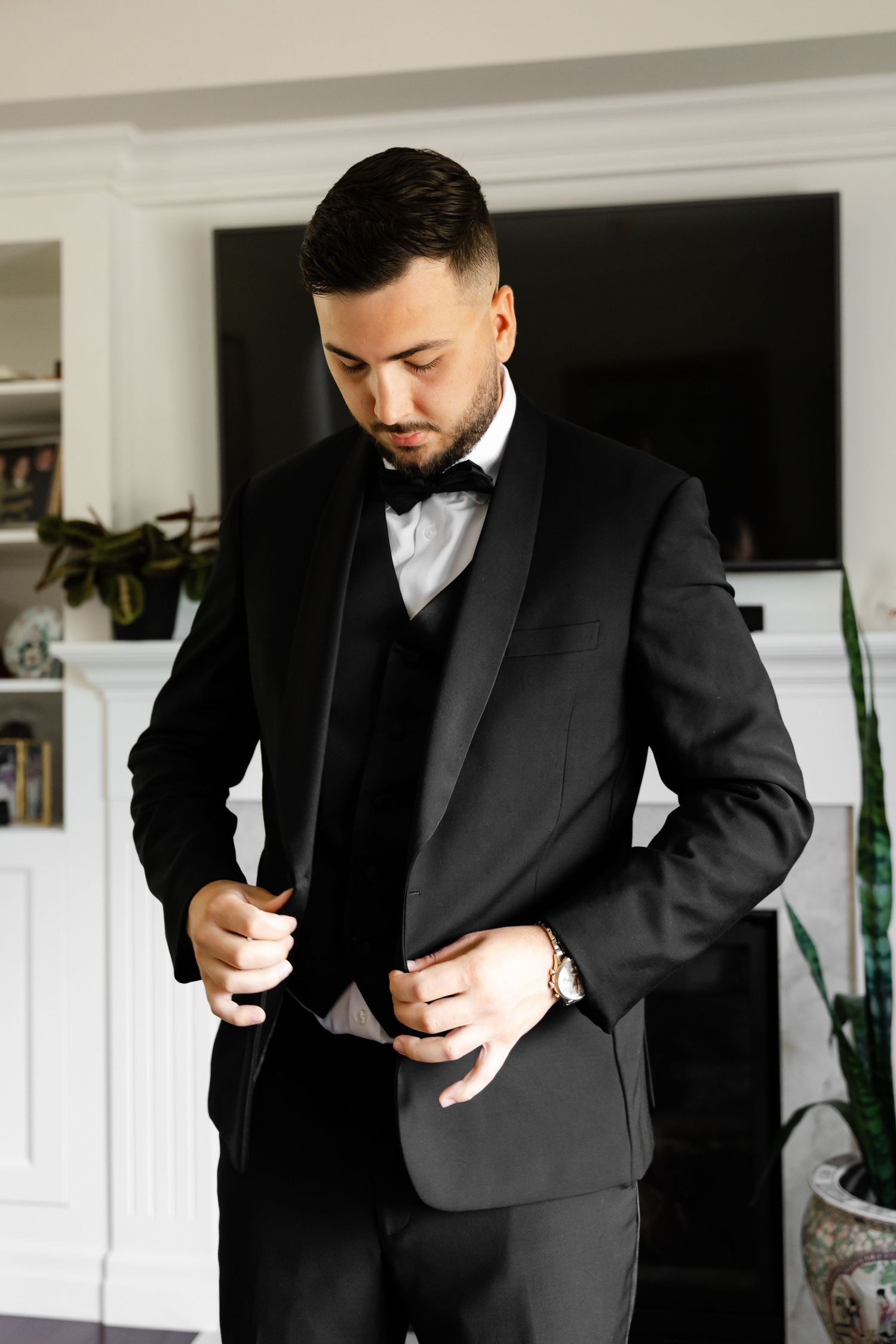 A groom adjusts his formal black tuxedo while getting ready for his wedding.