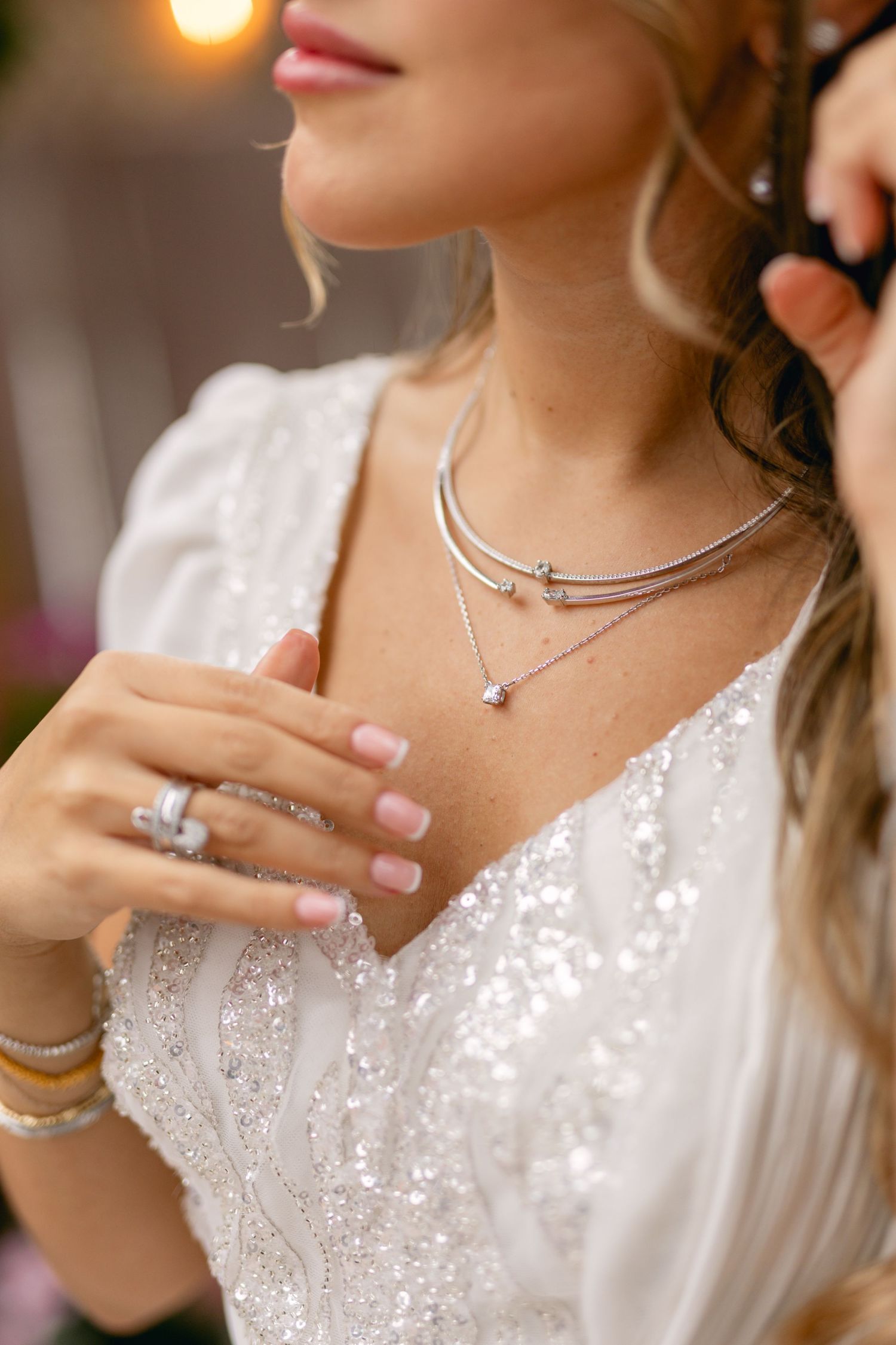 Detail shot of silver necklaces and jewelry on bride in white lace dress.