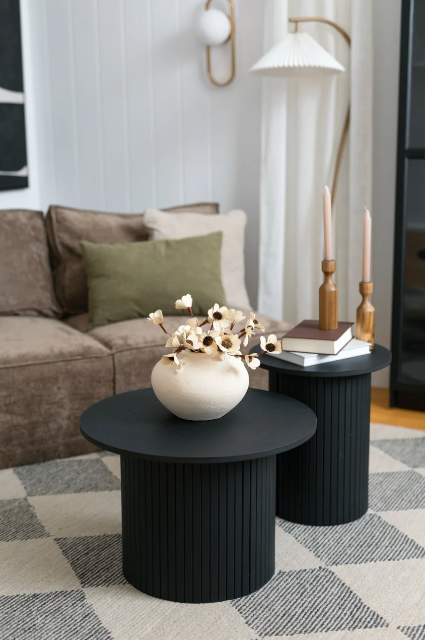 Modern black fluted coffee table set with white bowl on gray geometric rug in contemporary living room setting.