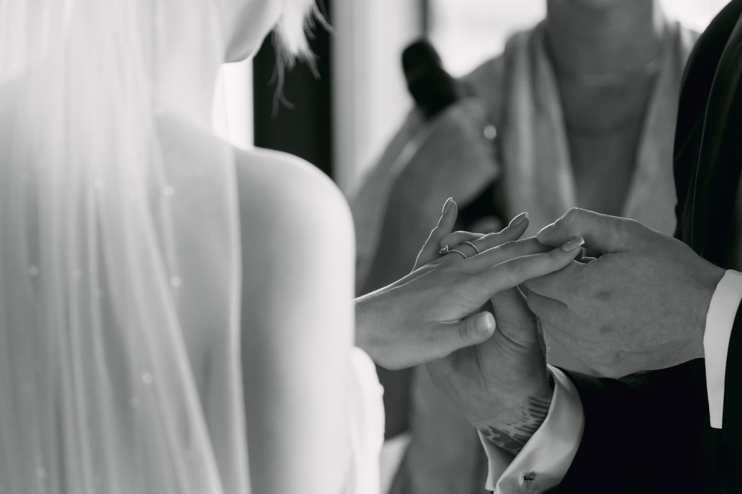 Black and white close-up of groom placing wedding ring on brides finger during ceremony.