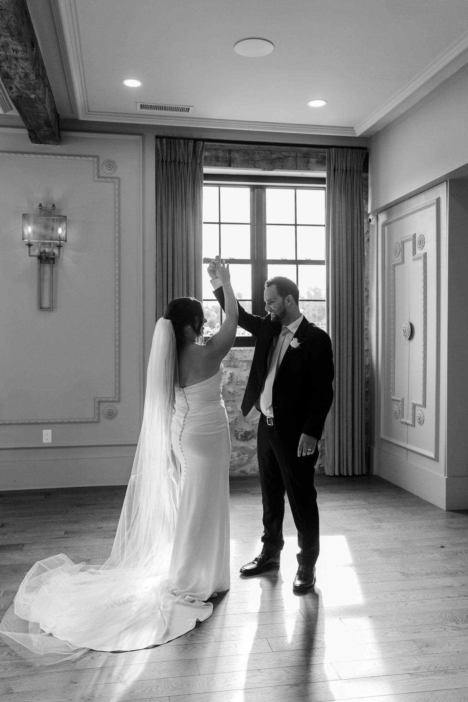 Black and white photo of bride and groom sharing private dance in sunlit elegant ballroom.