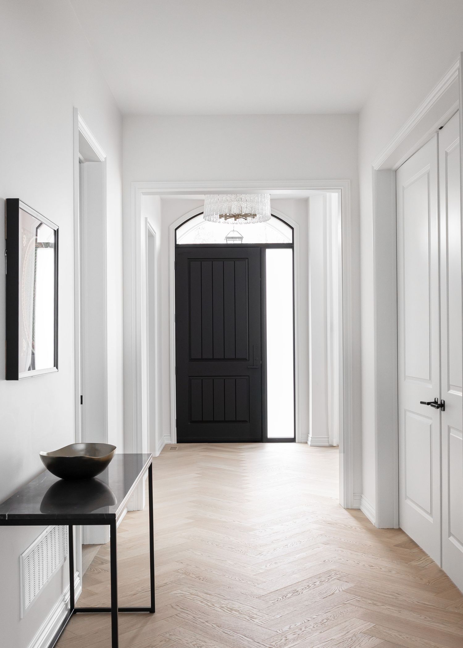 Long white hallway with herringbone wood flooring and black accent doors.