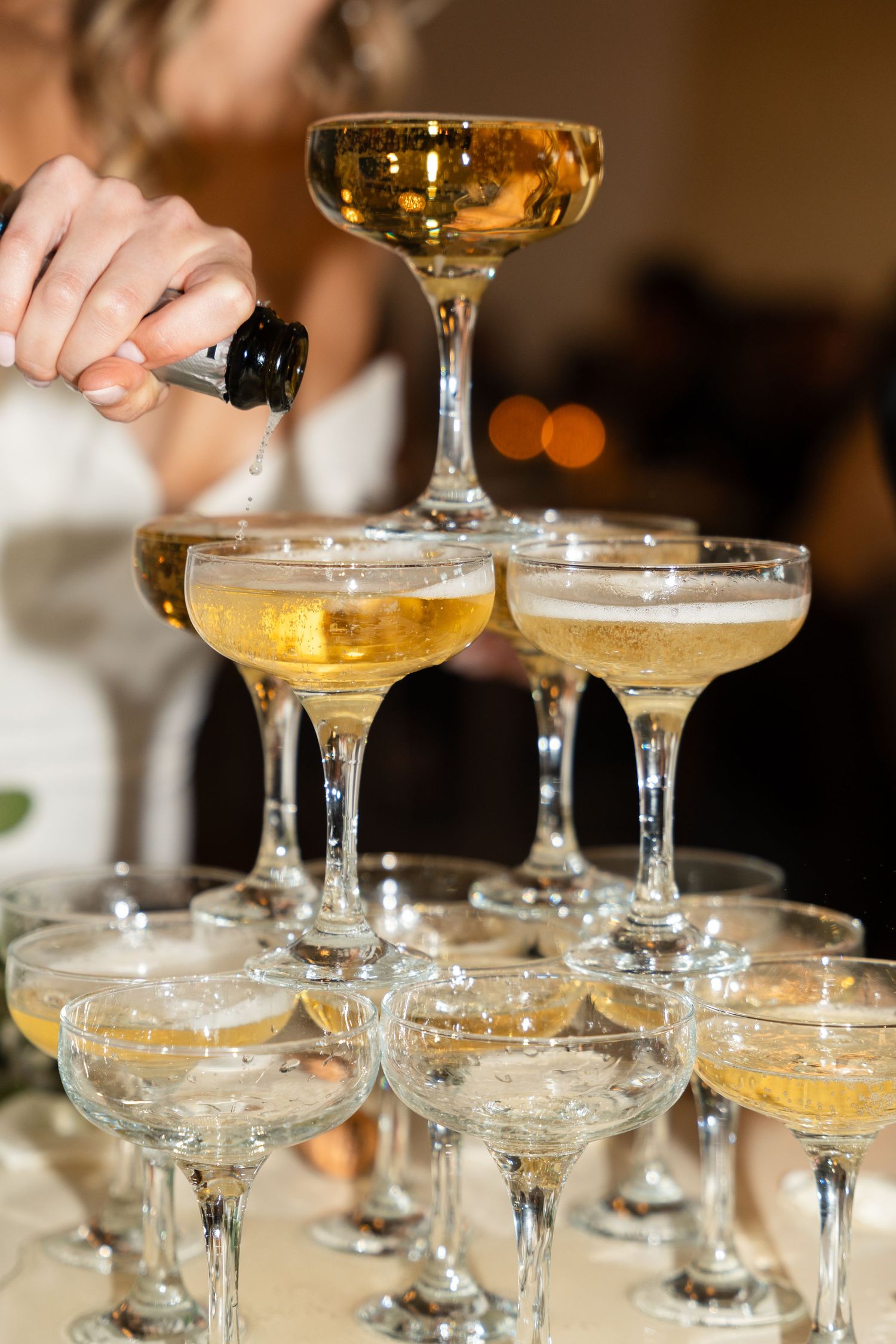 Close-up of champagne being poured into vintage coupe glasses arranged in a tower.