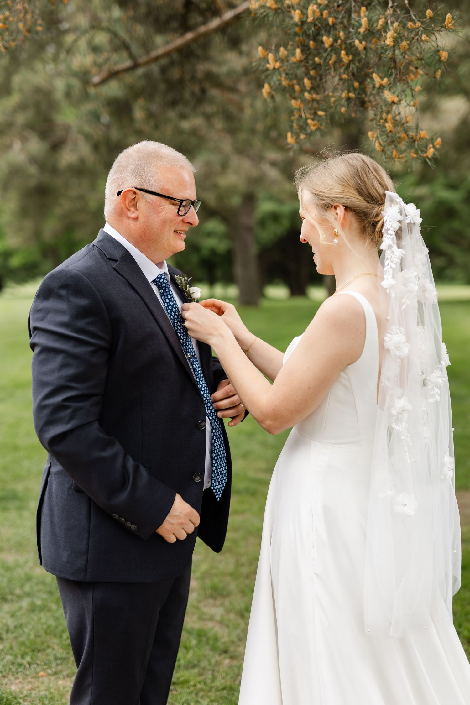 Emotional first look moment between a bride in white dress and someone in a navy suit outdoors.