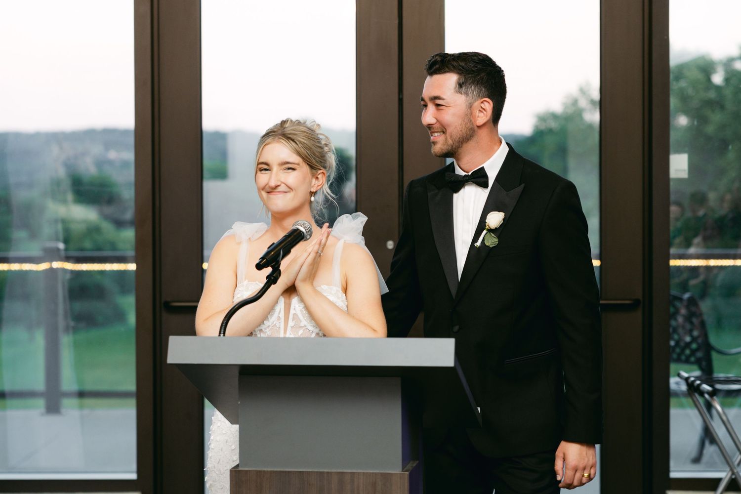 Wedding reception celebration with guests dancing in elegant venue with floor-to-ceiling windows.