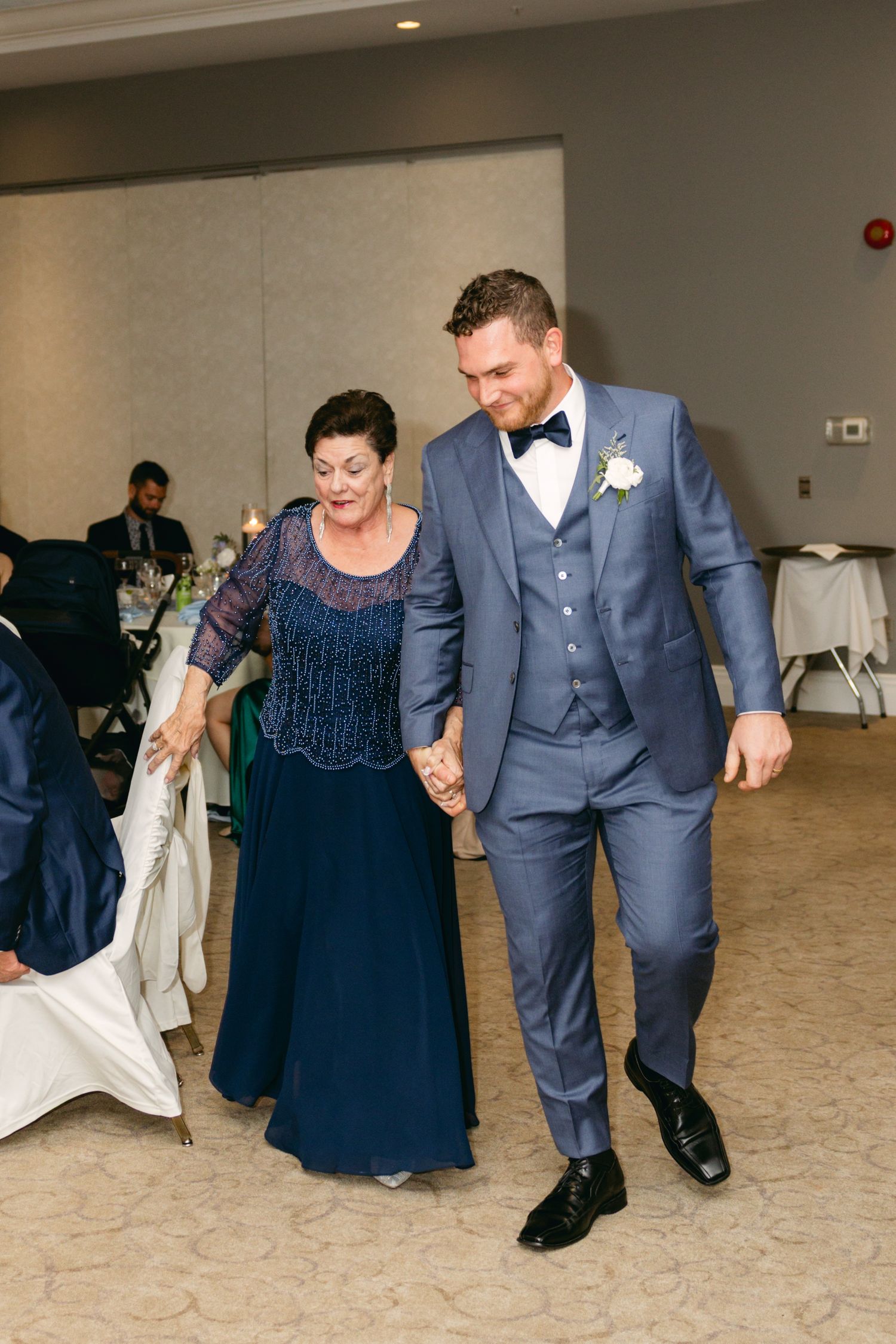 Dancing couple in navy and grey formal attire moving across elegant ballroom floor.