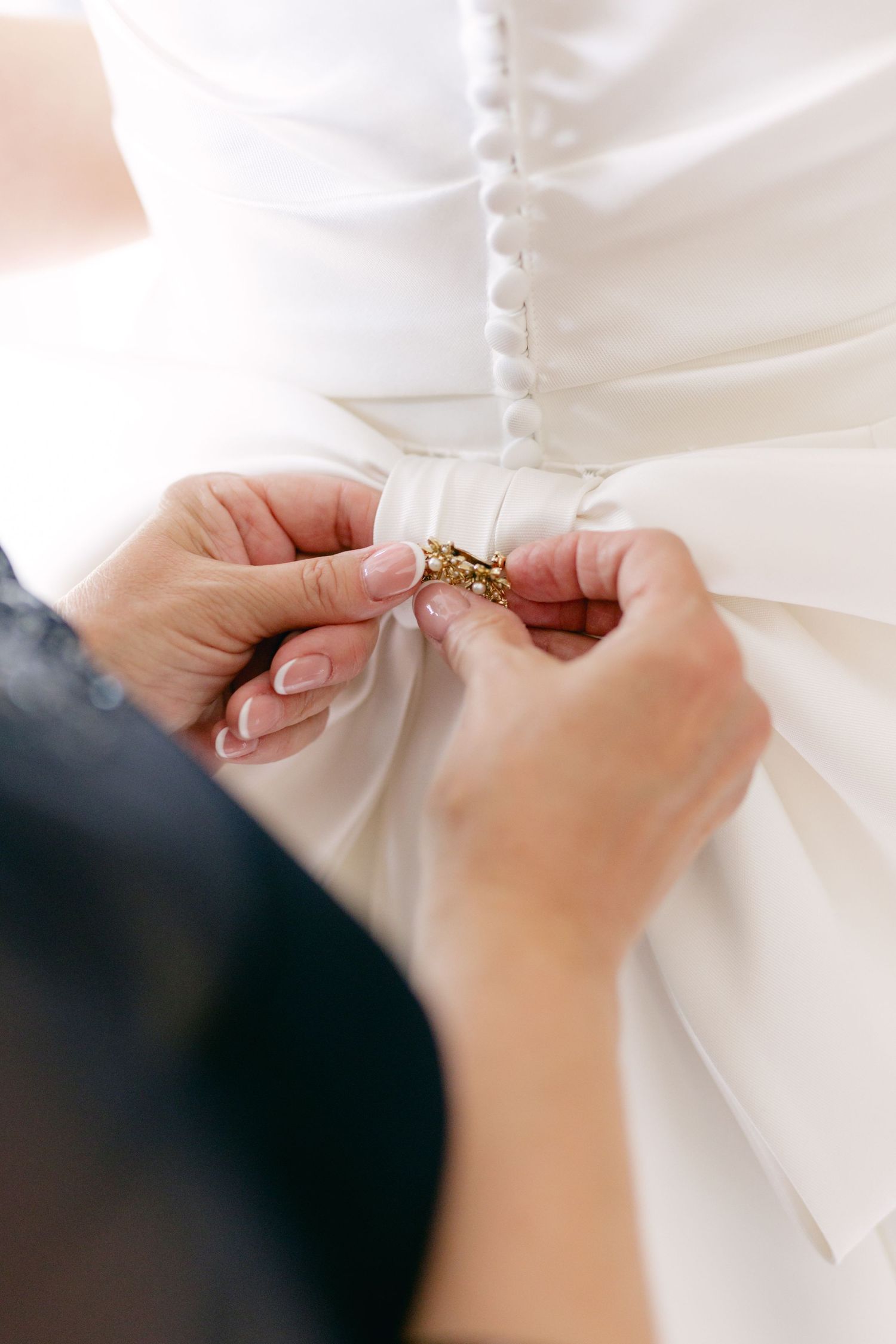 Close-up shots of hands buttoning up the back of a white wedding dress.