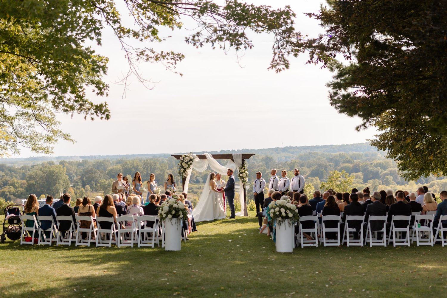 Outdoor wedding ceremony setup with white chairs arranged in rows on a scenic hilltop during golden hour.