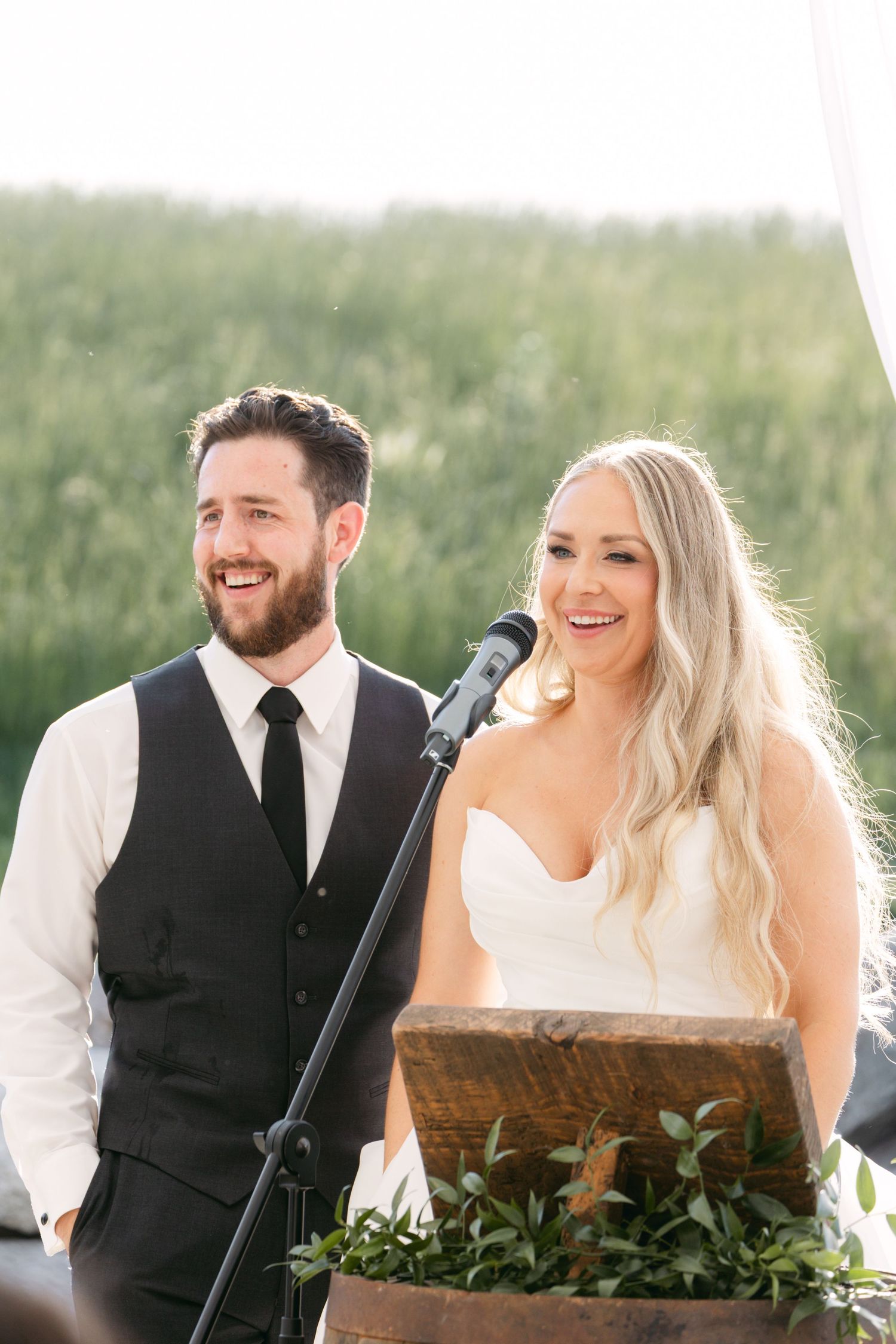 Wedding party members share joyful moment at rustic wooden podium during reception.