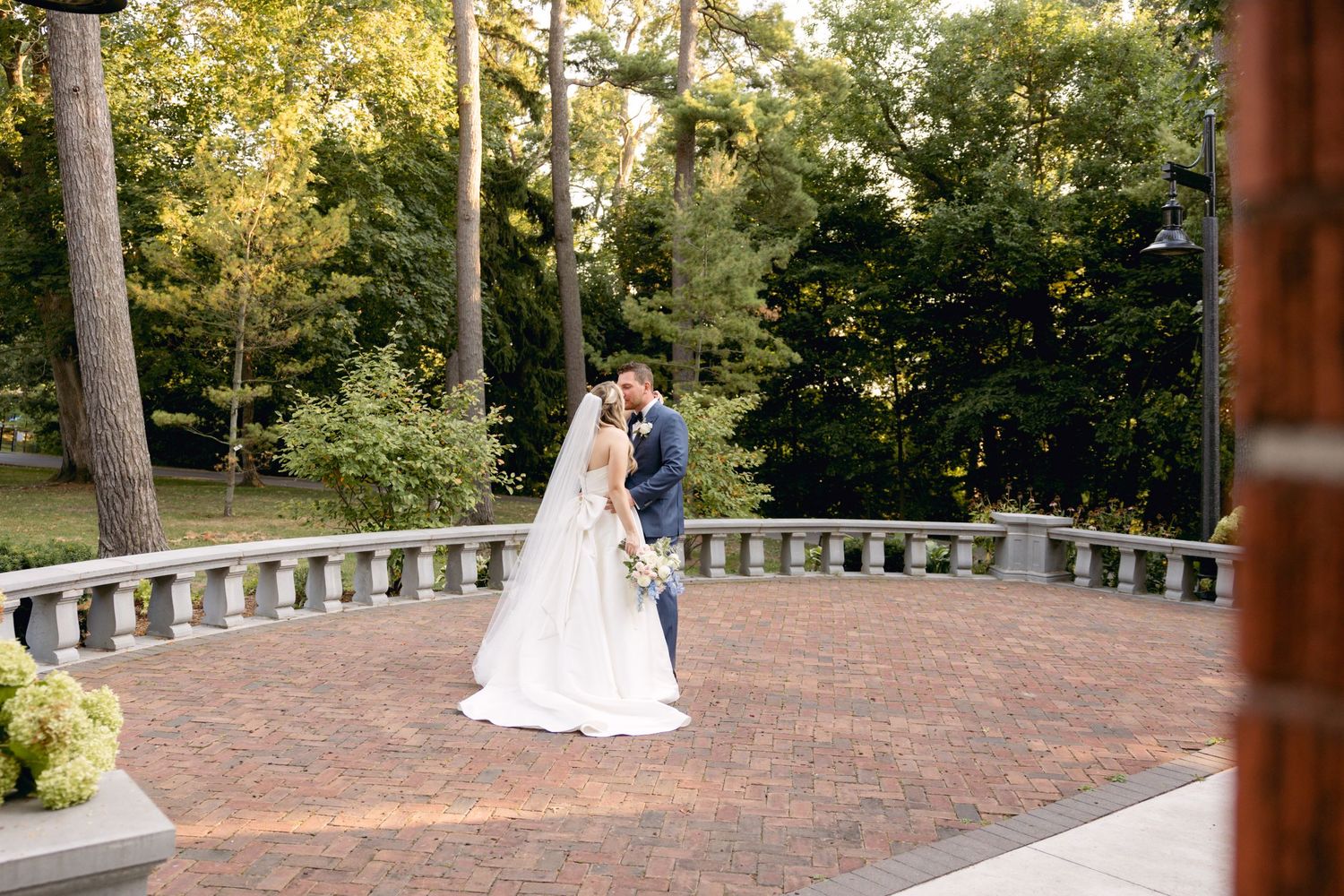 Panoramic view of a brick patio wedding venue with stone railings surrounded by lush greenery.