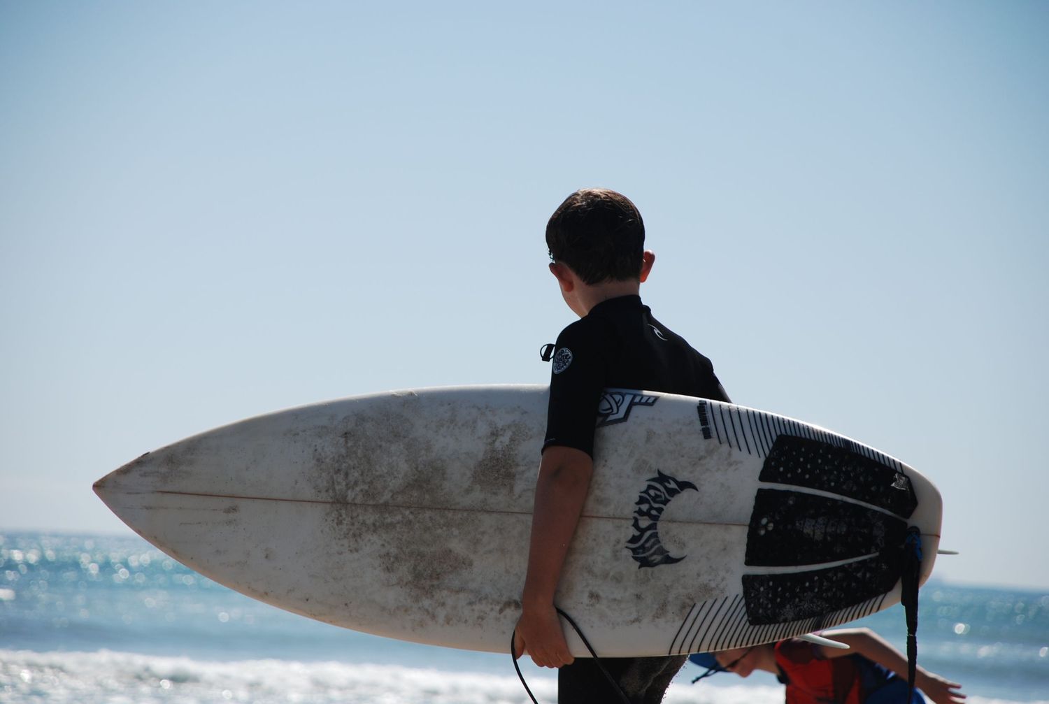 Young boy standing on the beach holding a surfboard under his arm