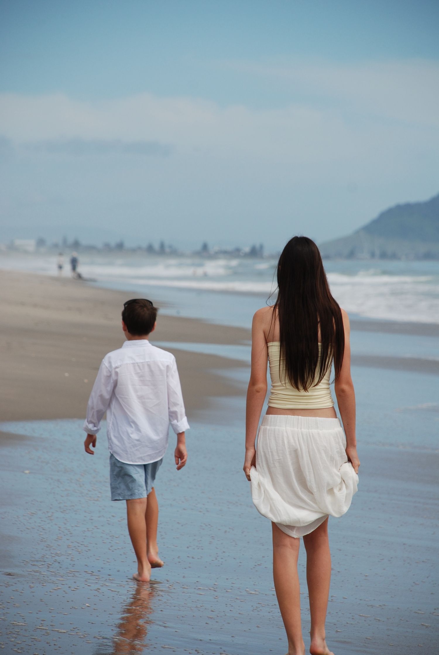Candid moment of siblings enjoying a beach walk, photographed from behind